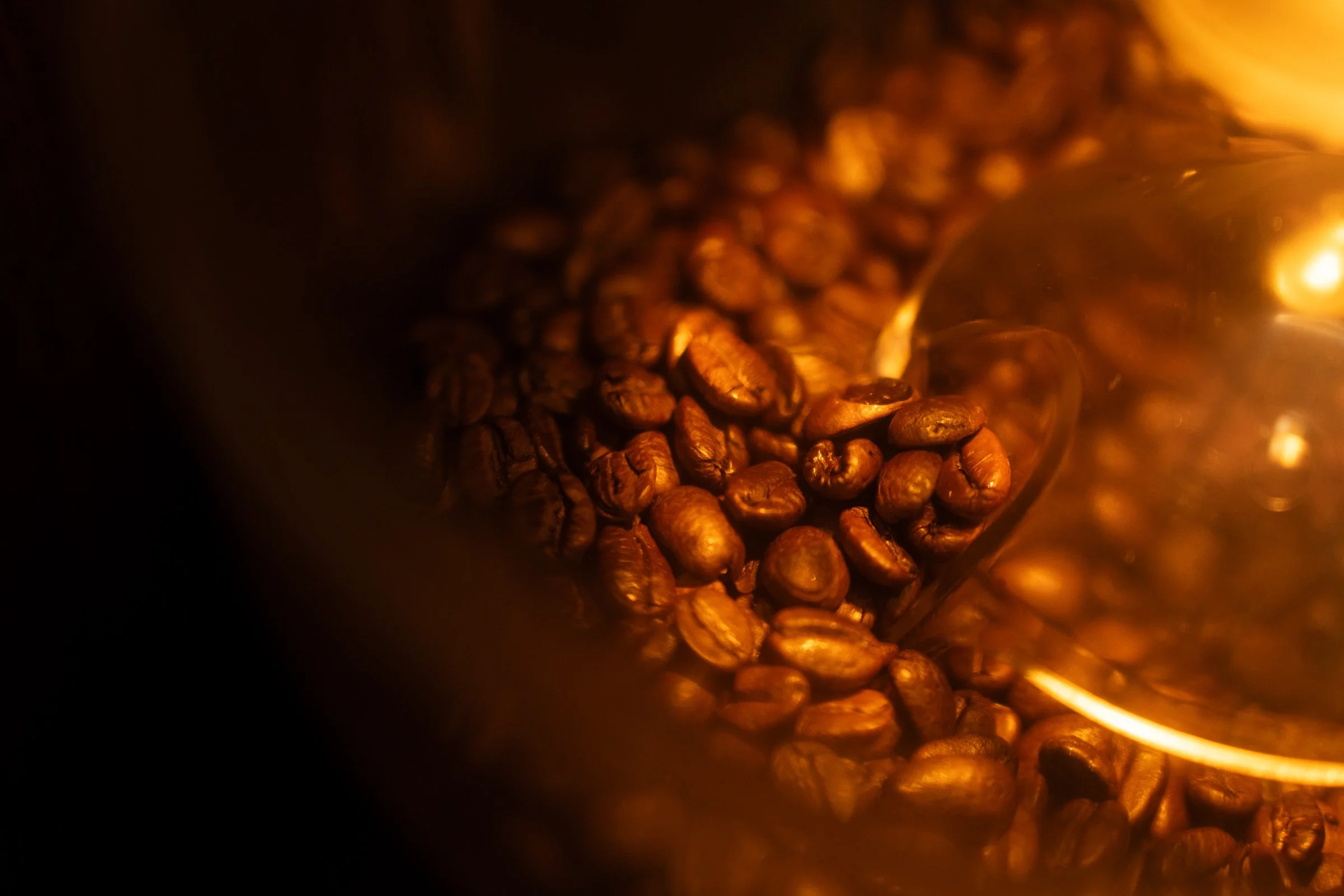 Close-up of roasted coffee beans with a glass container reflecting light, capturing a warm, dark, and rich atmosphere.