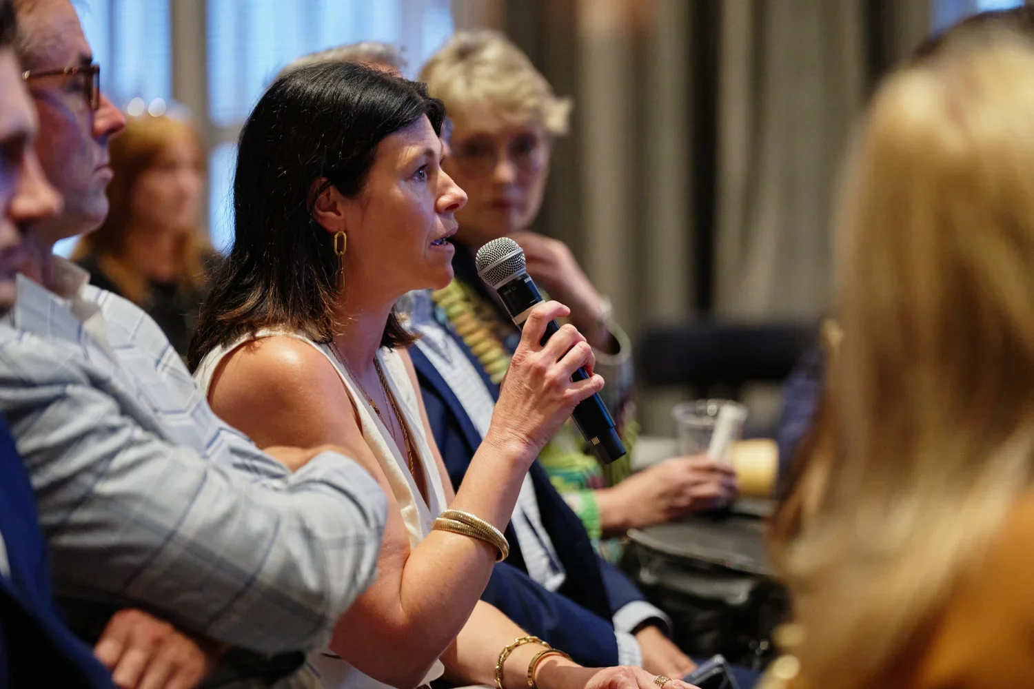 A woman with dark hair and gold earrings speaking into a microphone during a panel discussion at a conference.
