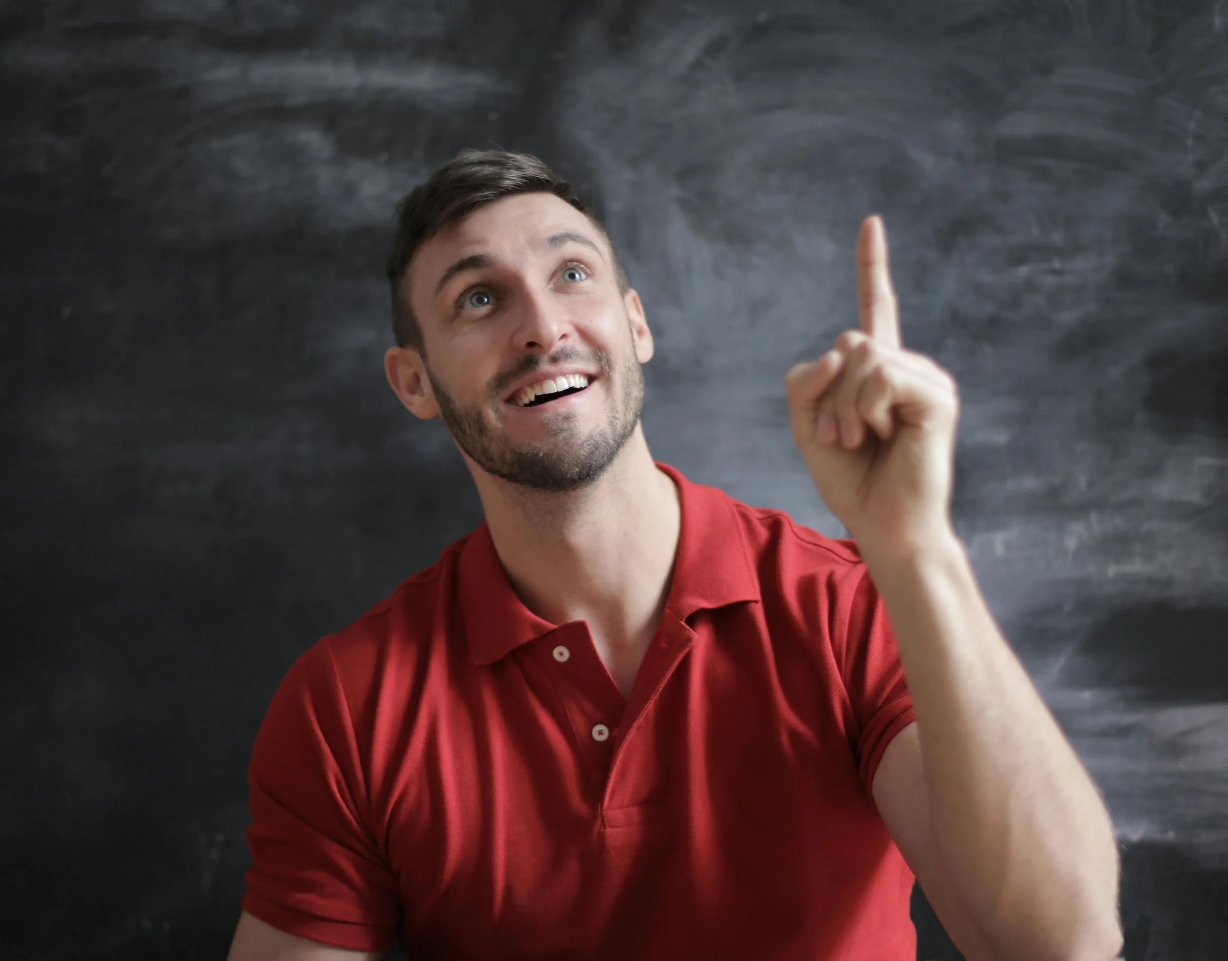 Man in red shirt pointing up in portrait with a black and grey background