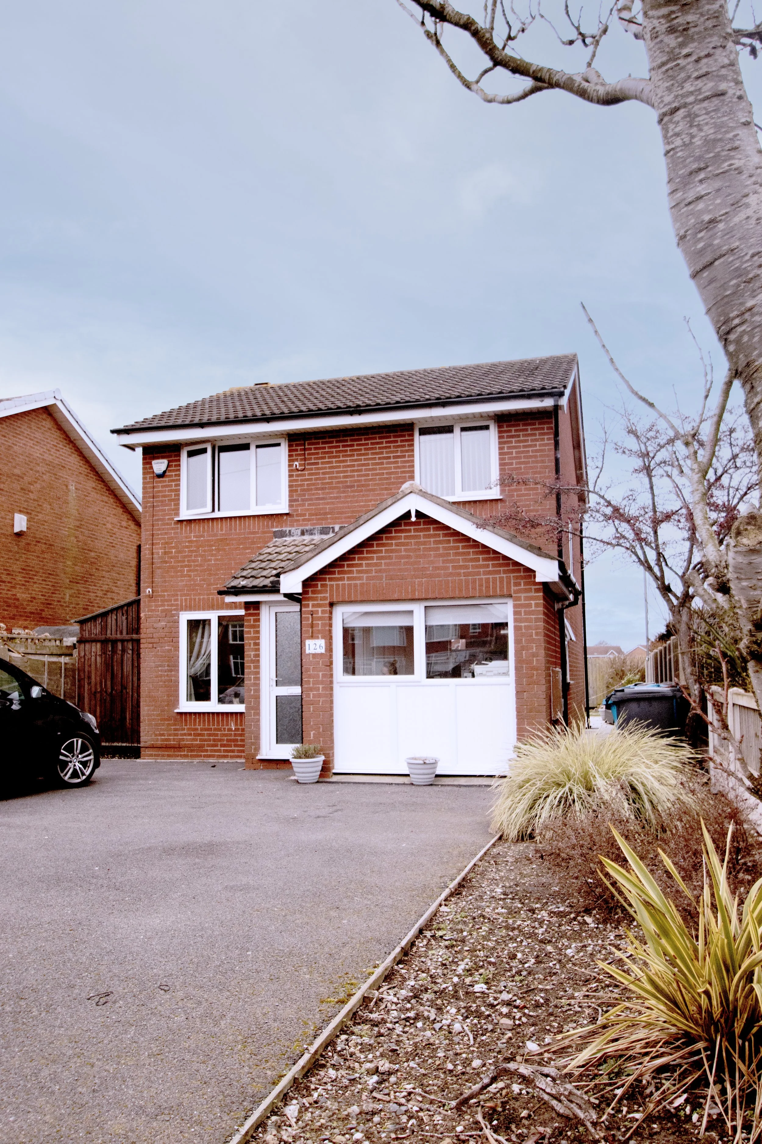 A two-story brick house with a white garage door, potted plants near the entrance, and a driveway.