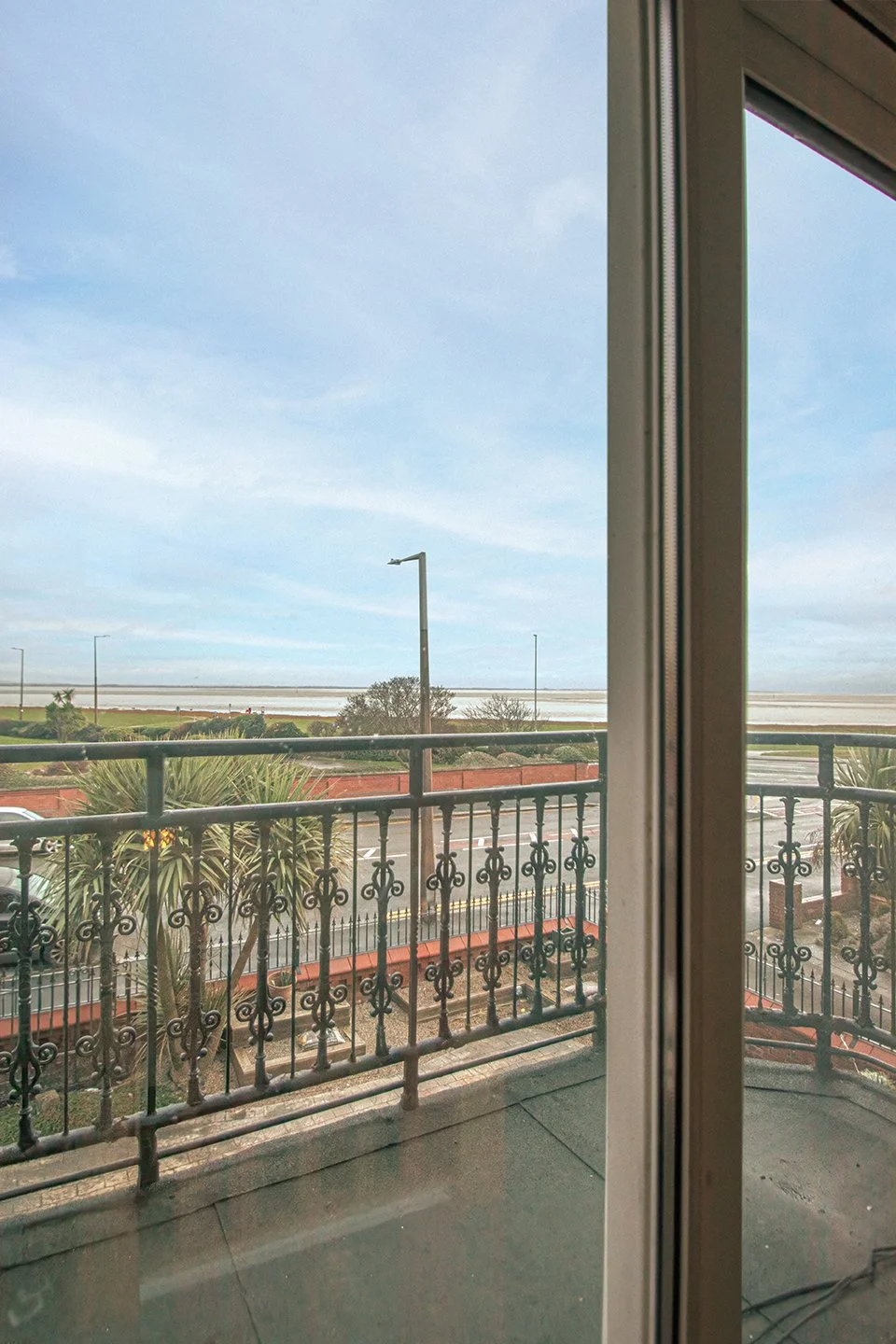 View from a balcony looking out over a road, with a railing and some trees, and a large body of water or salt flats in the distance, under a cloudy sky.