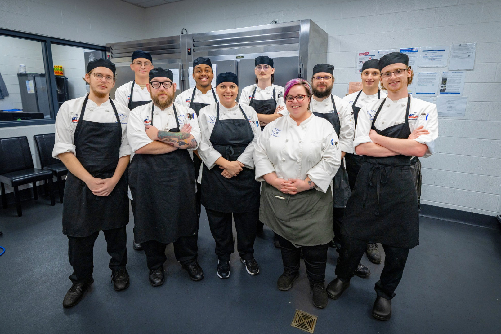 Group of professional chefs and kitchen staff in uniform, standing together in a commercial kitchen.