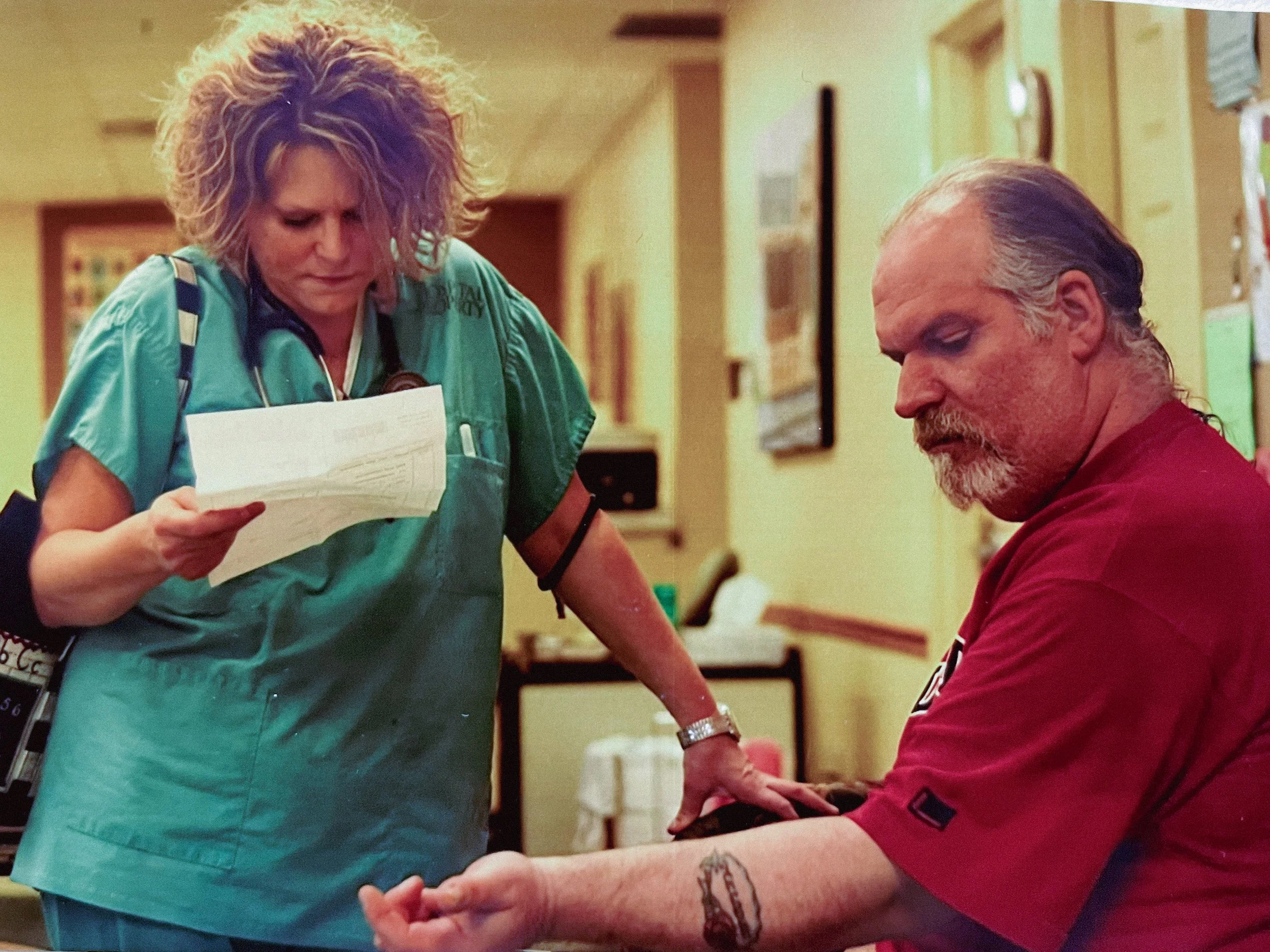 A healthcare professional, wearing green scrubs and a stethoscope, is standing next to a patient in a medical setting.