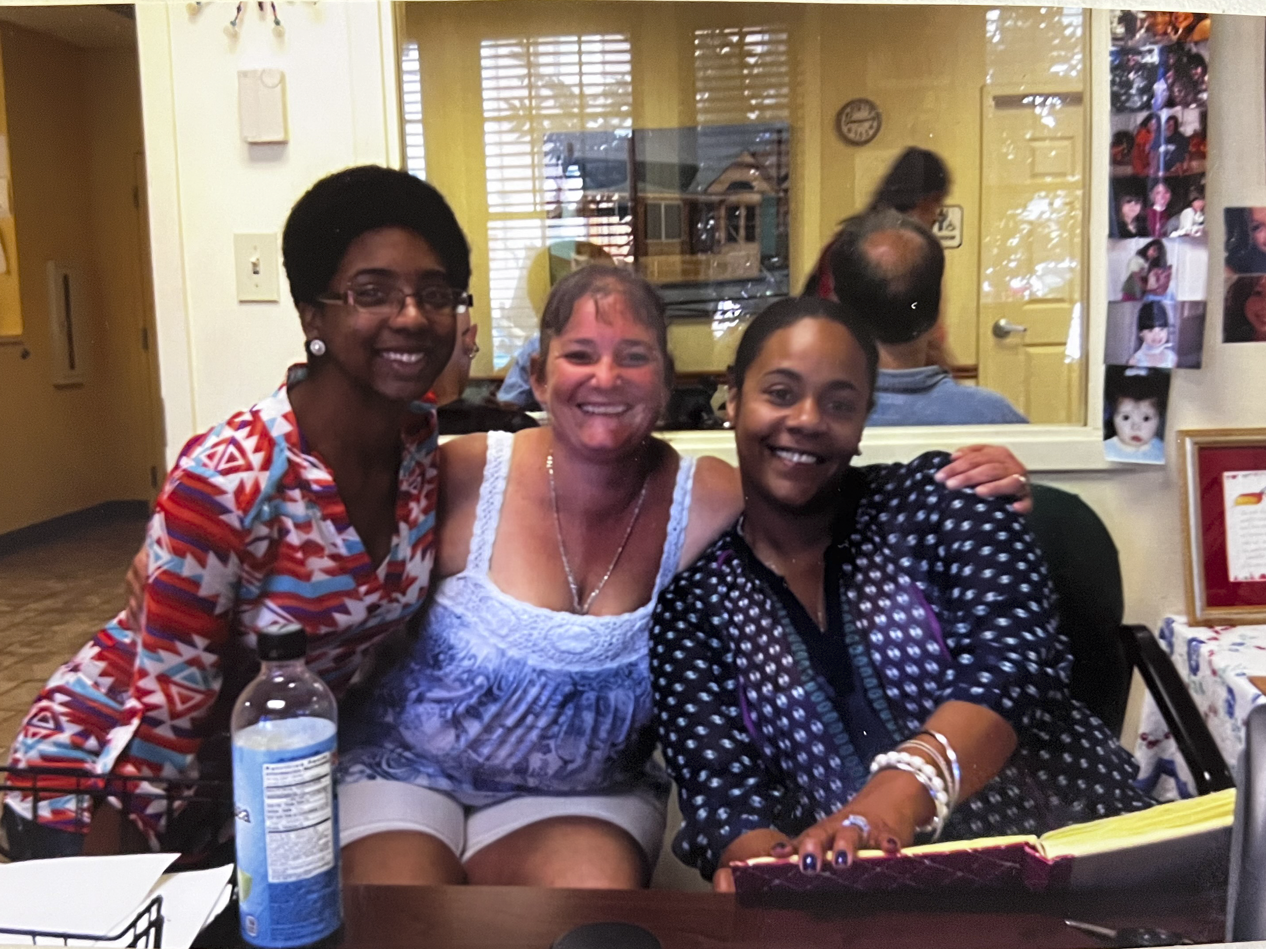 Three women smiling and sitting at a table in an indoor setting.