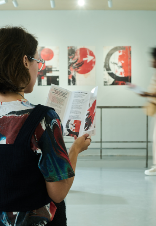 Person reading a brochure at an art gallery with abstract artwork on the wall behind.