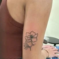 Tattoo of a flower with a bee in the center on a person's upper arm.