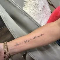 Close-up of a person's forearm with a delicate tattoo in cursive script reading 'the sky for the storm'