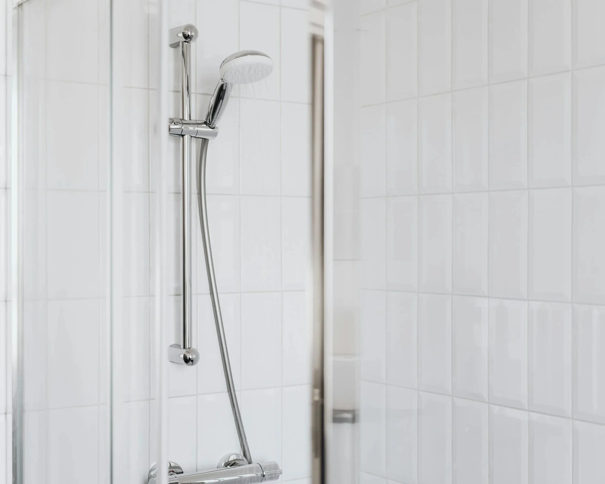 Close-up of a chrome shower head and support rail in a white tiled shower.