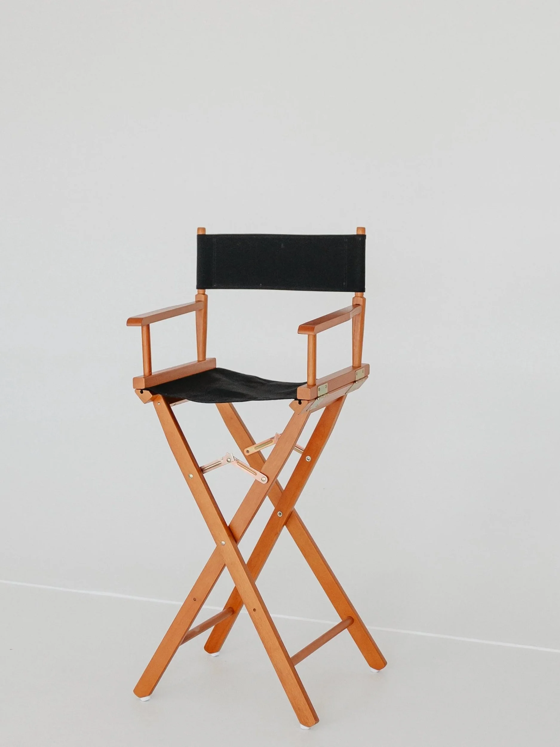 A black director's chair with a wooden frame and white feet, set against a plain white wall.