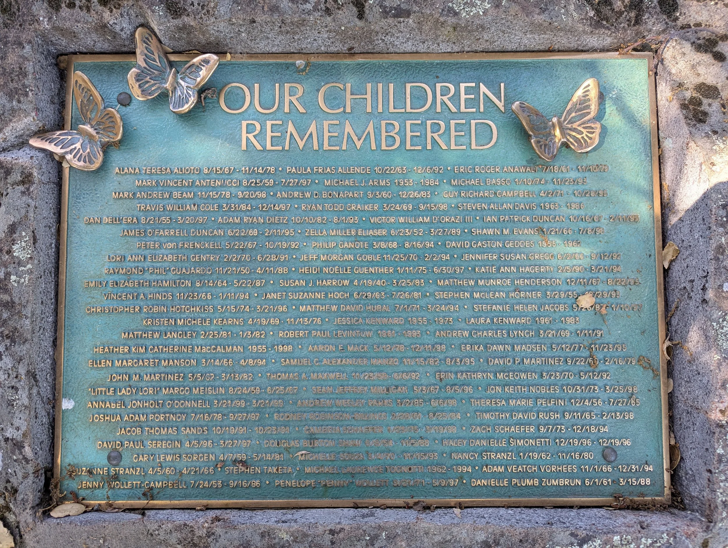 A memorial plaque with butterflies attached to it, inscribed with the names and dates of children who have passed away.