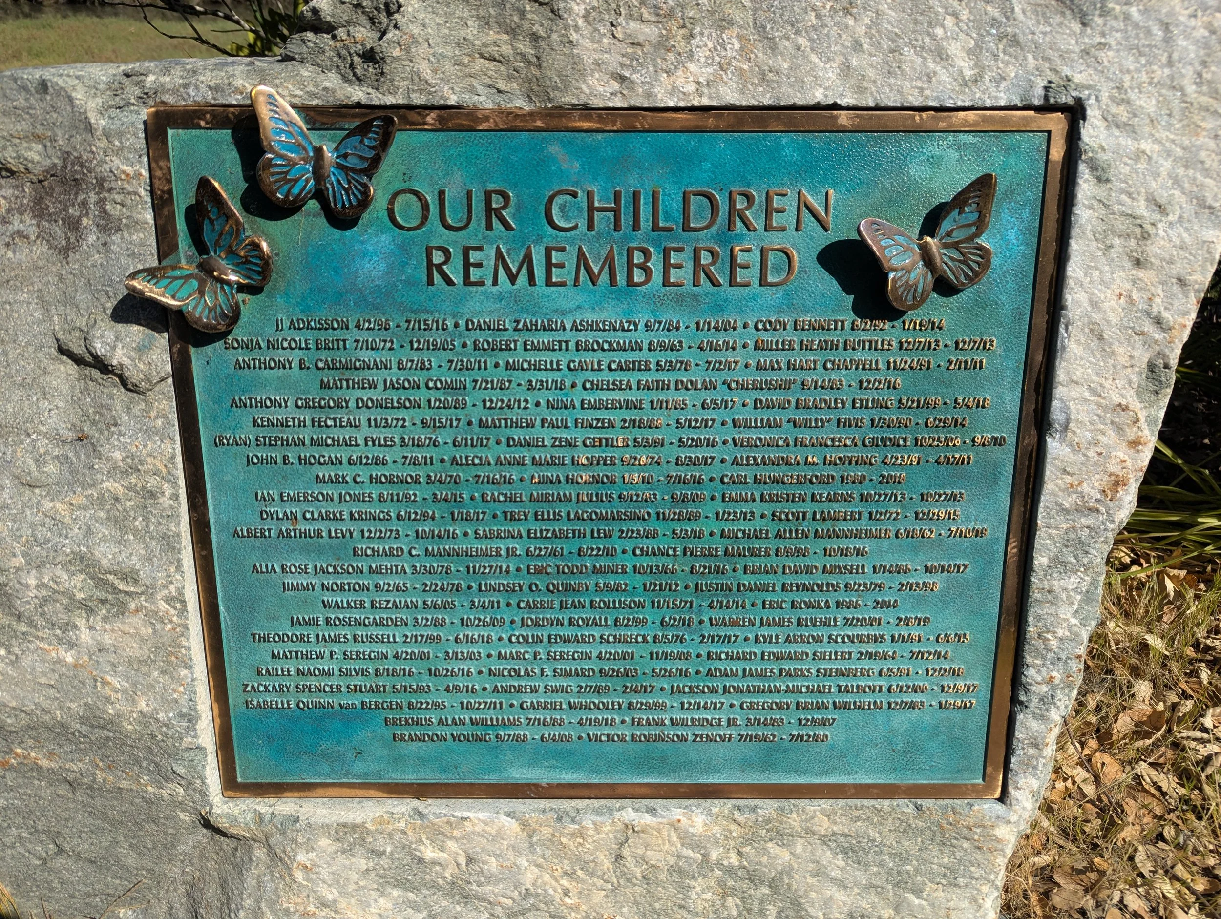 A memorial plaque mounted on a stone wall with decorative butterfly accents, honoring children who have died.
