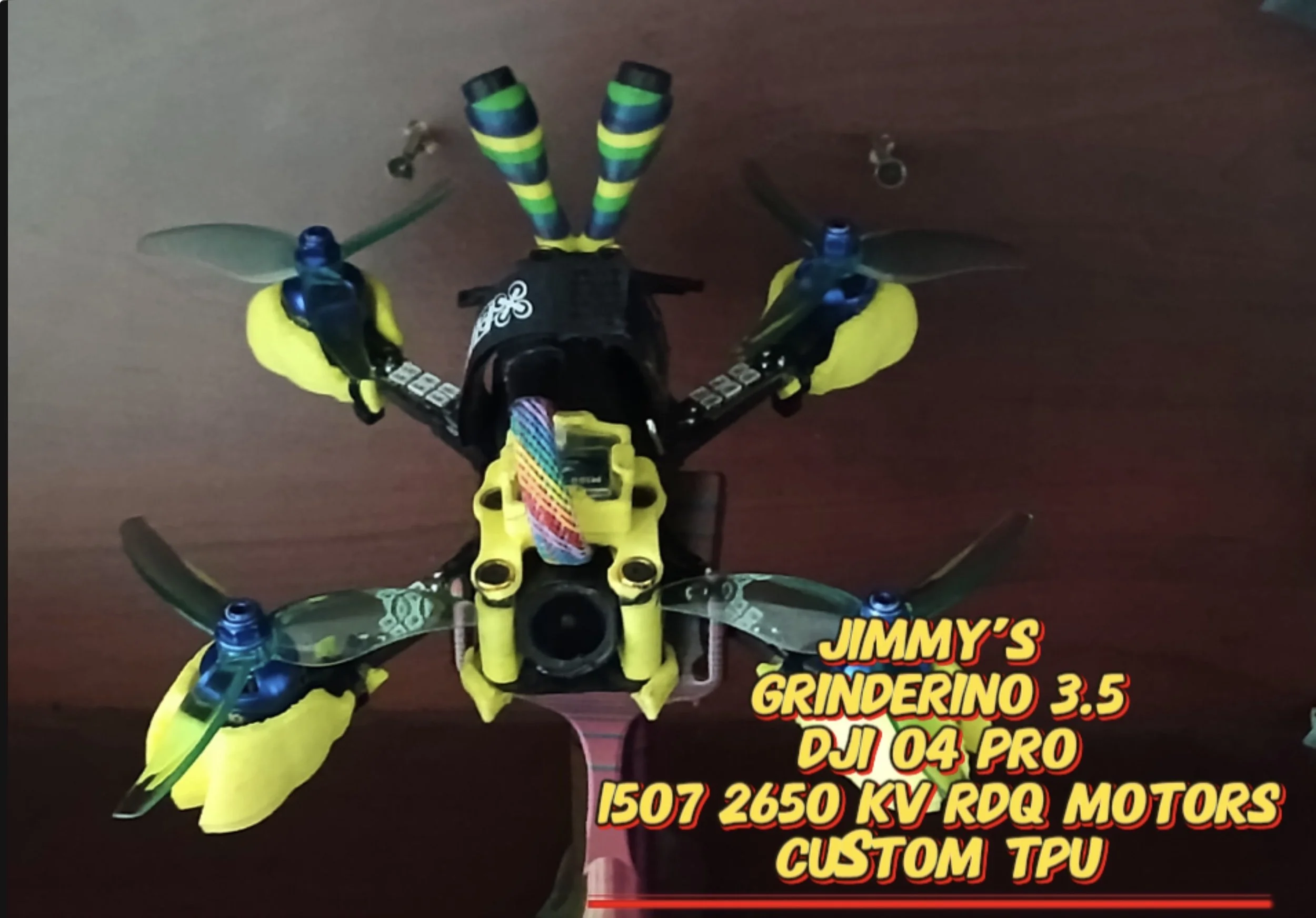 A custom drone with yellow and black components, blue motors, and multicolored wiring, placed on a wooden surface, with text overlay describing its specifications and parts.