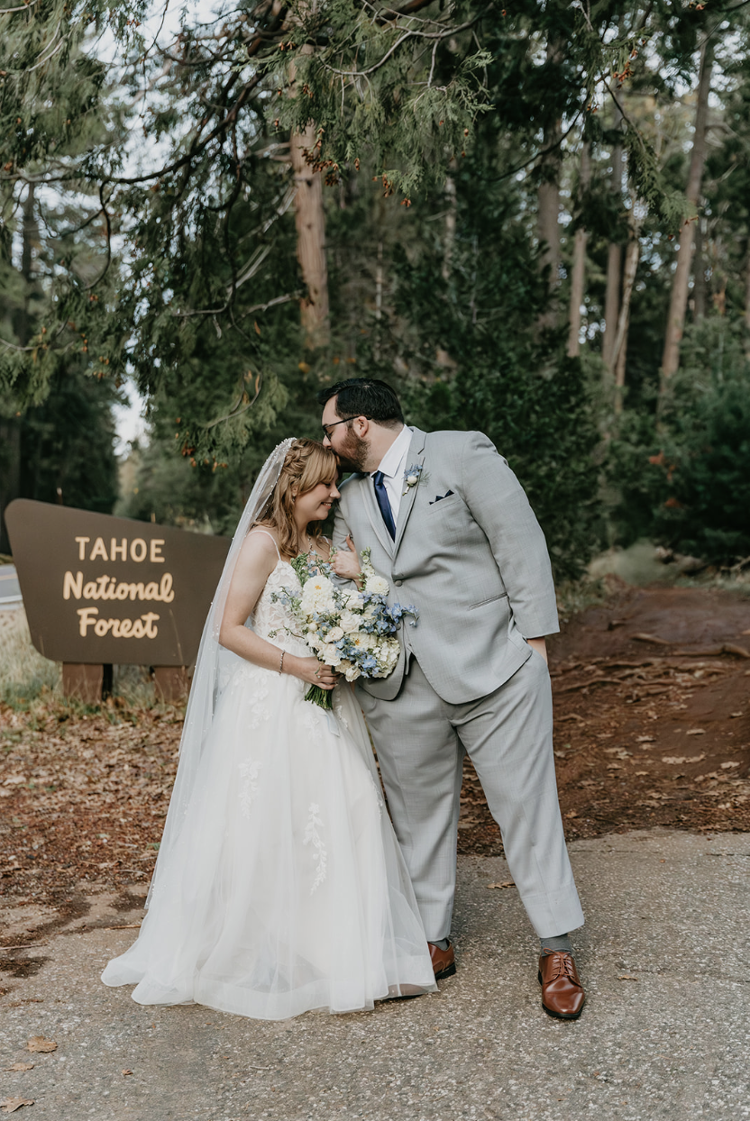 Bride and groom sharing a tender moment in front of a sign that reads 'Tahoe National Forest', with trees in the background.