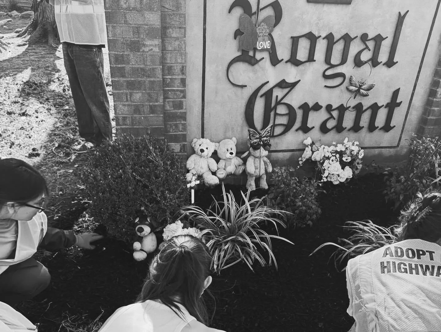 People laying flowers and placing stuffed animals at a memorial site with a sign that reads 'Royal Grant,' decorated with butterflies and flowers.