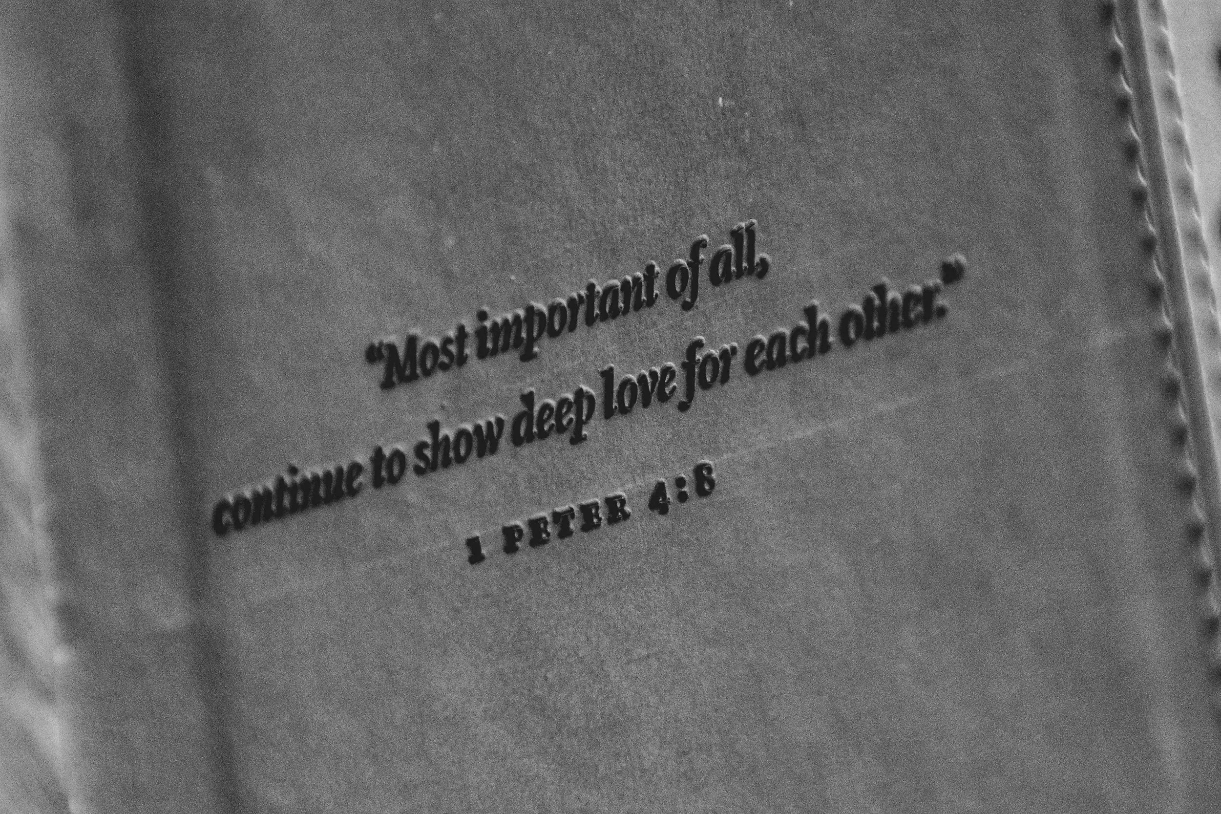 Close-up of a metallic surface with engraved Bible verse from 1 Peter 4:8, reading 'Most important of all, love each other.'