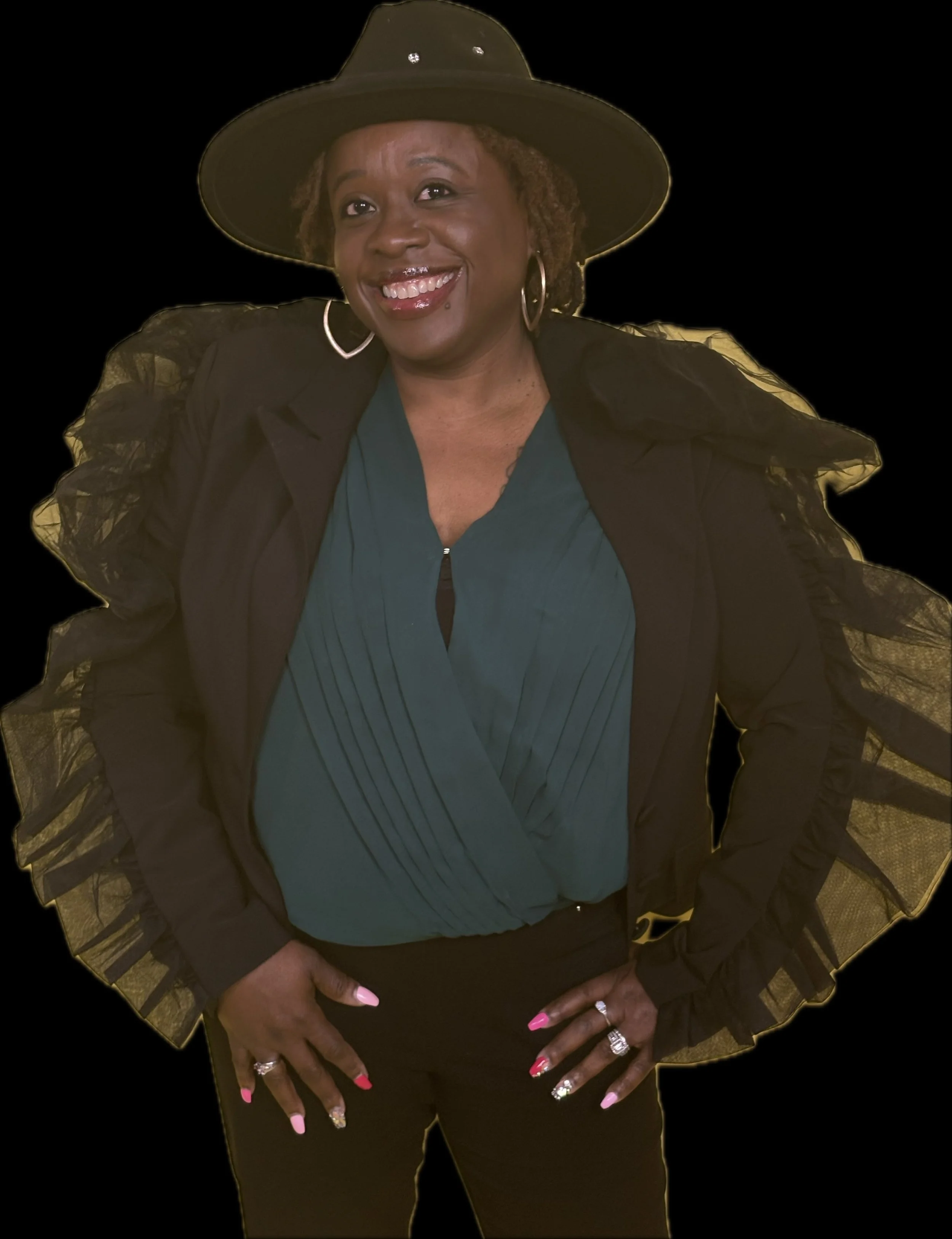 A woman wearing a black wide-brimmed hat with decorative accents, a teal blouse, and a black jacket with ruffled sleeves, standing confidently with her hands on her hips and smiling.