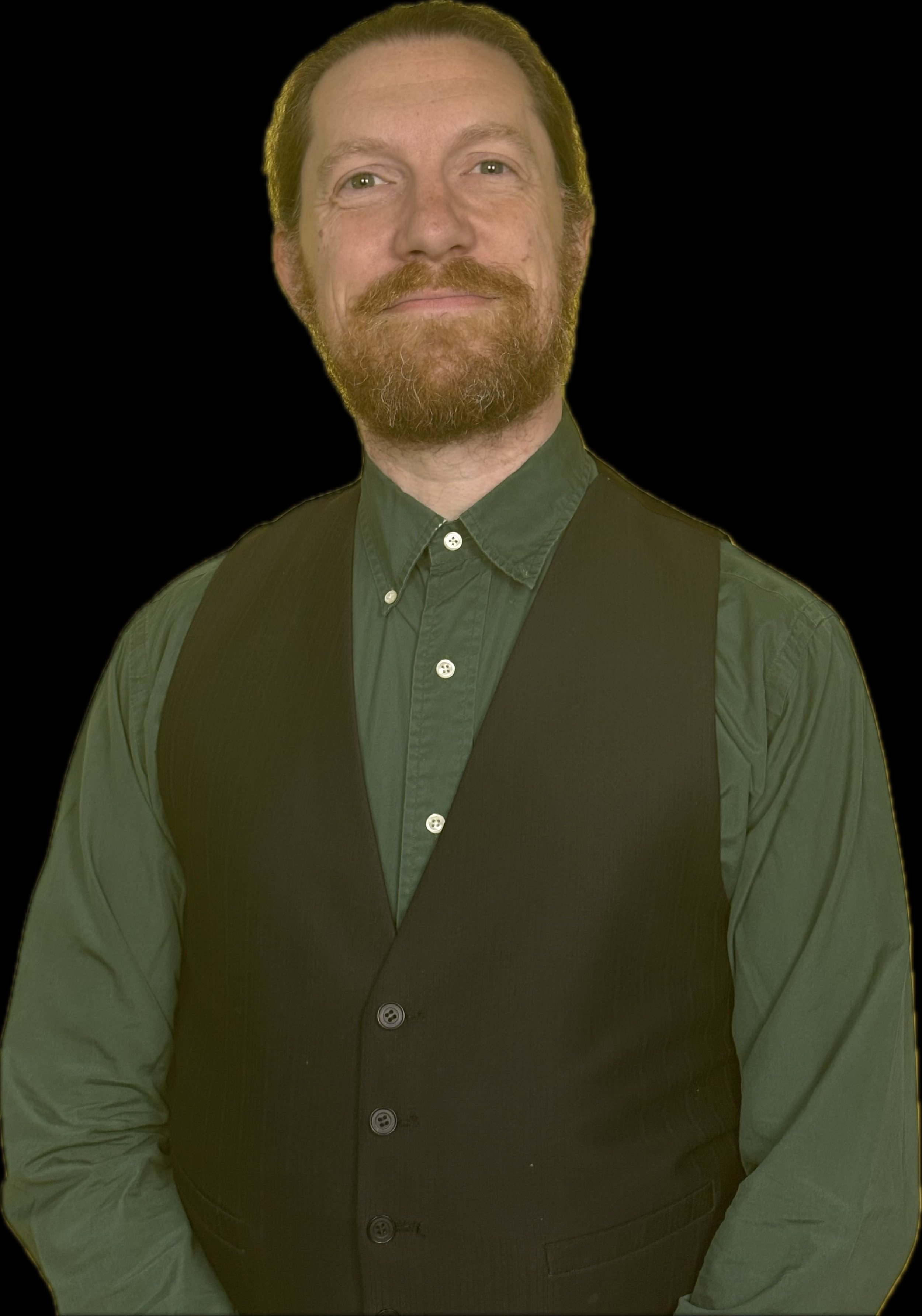 A man with a beard and mustache, wearing a dark vest over a green button-down shirt, standing against a solid black background.