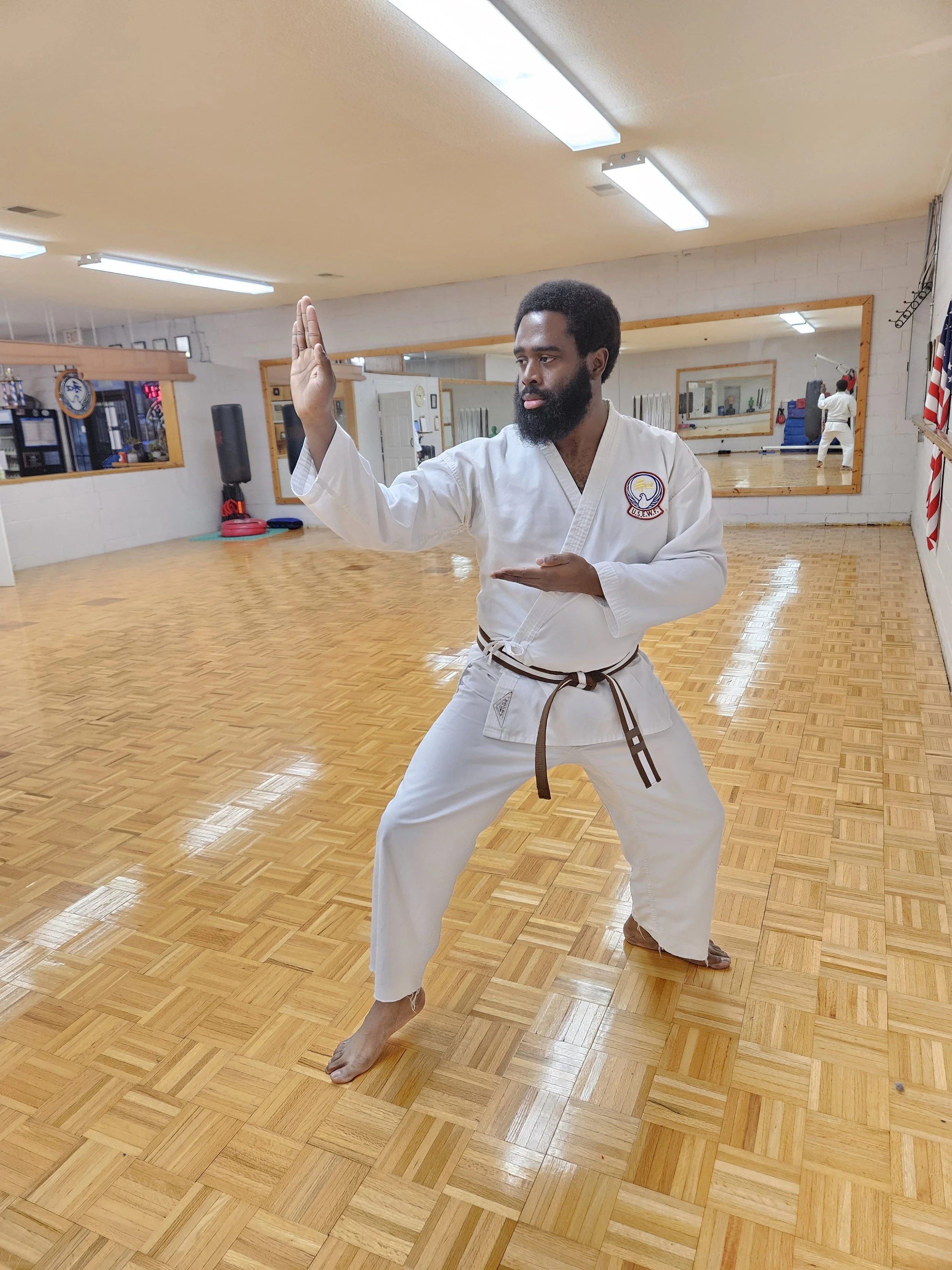 A man with a beard in a martial arts uniform practicing a karate stance in a dojo.
