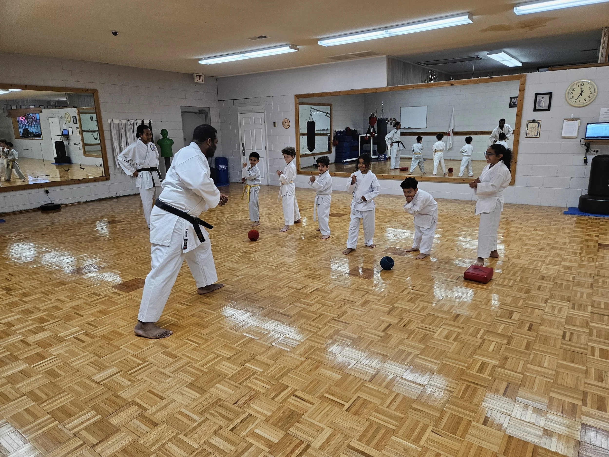Kids in karate uniforms standing in line with an instructor in a dojo, practicing martial arts.
