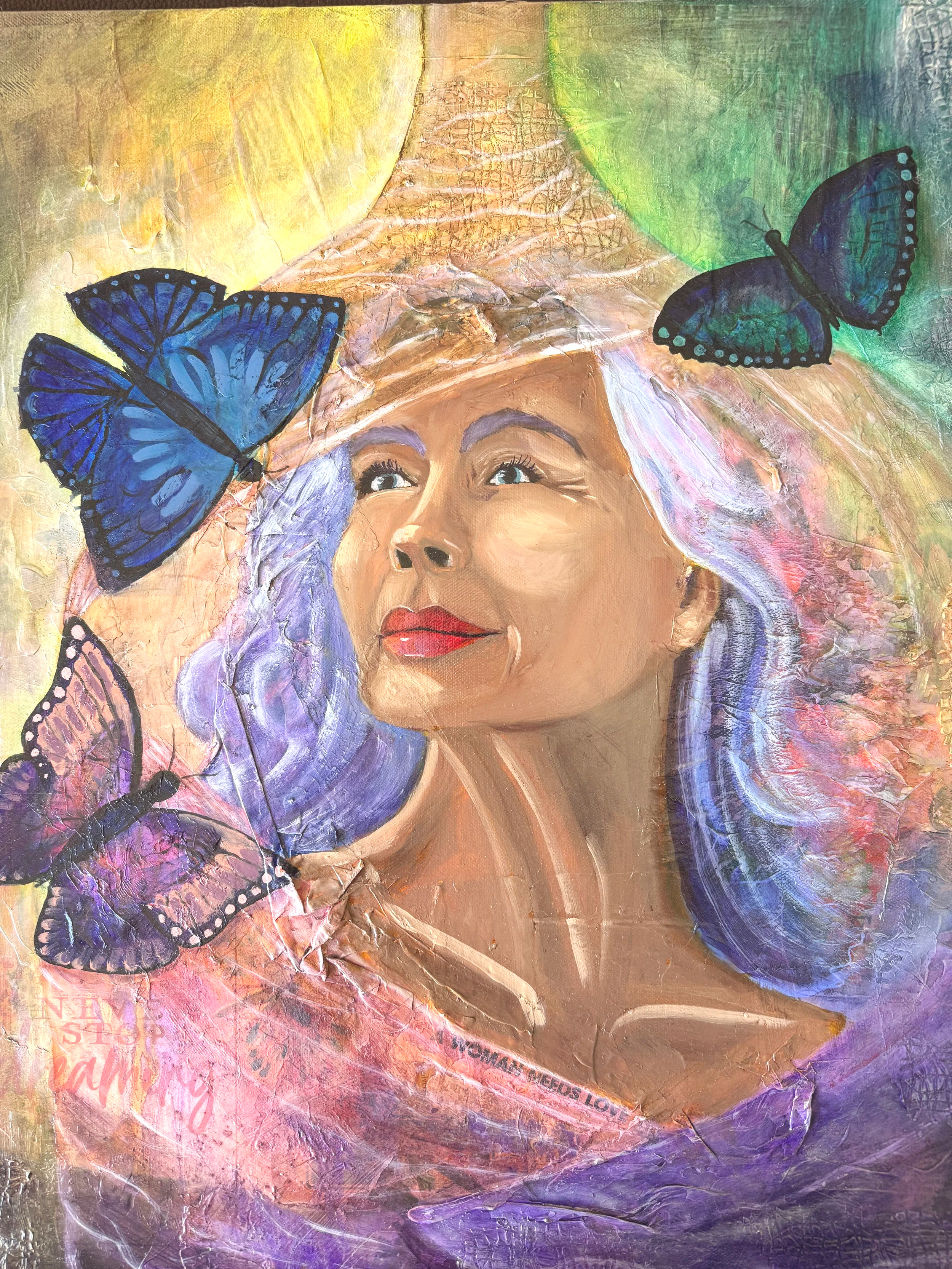 A painting of a woman with long, flowing hair emerging from a cocoon. Three butterflies are flying around her. The background consists of warm colors like yellow, pink, and orange, with pink, green and purple accents.