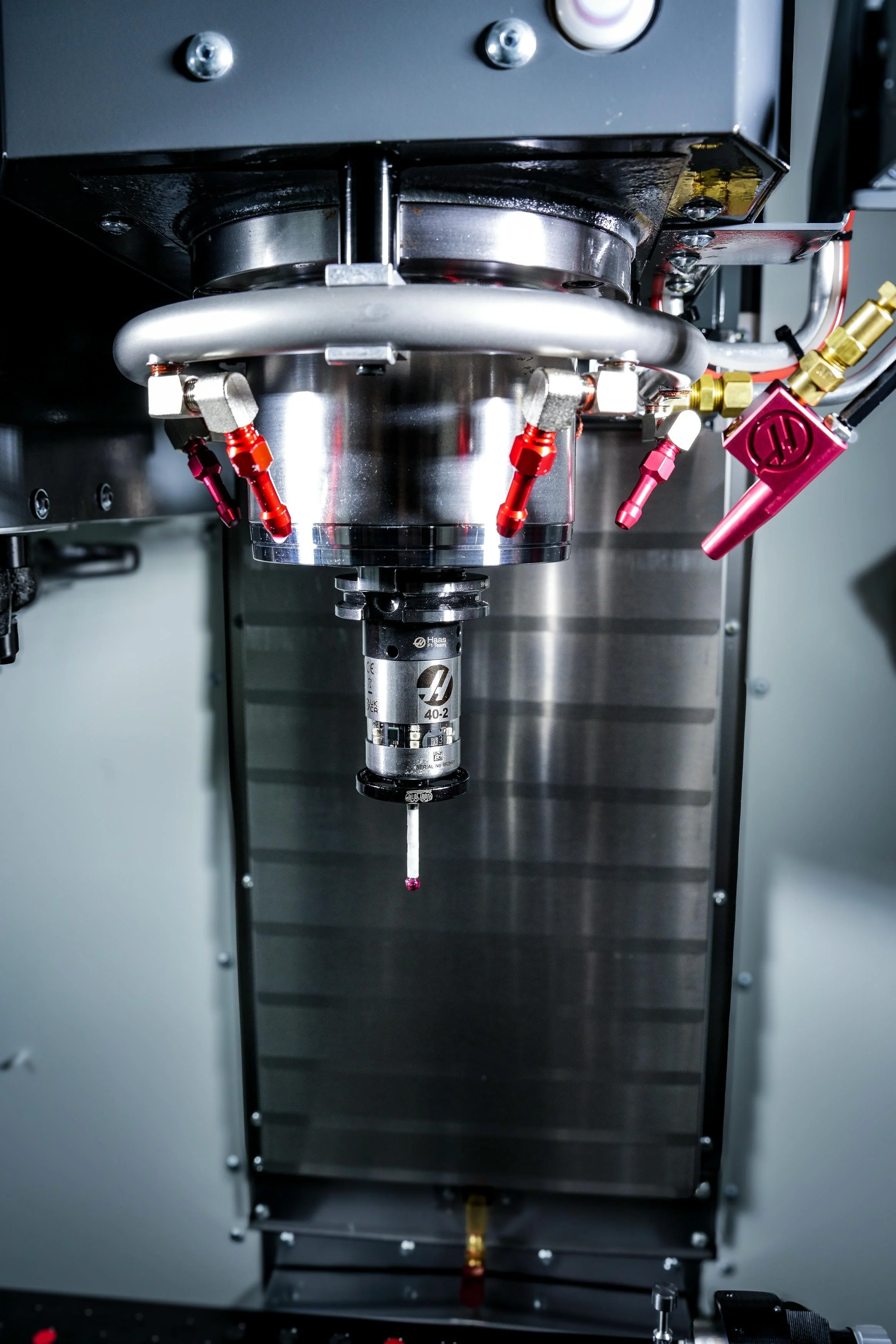 A close-up view of a scientific laboratory instrument with various metallic parts, red and gold fittings, and tubing, likely used for high-precision experiments or manufacturing processes.