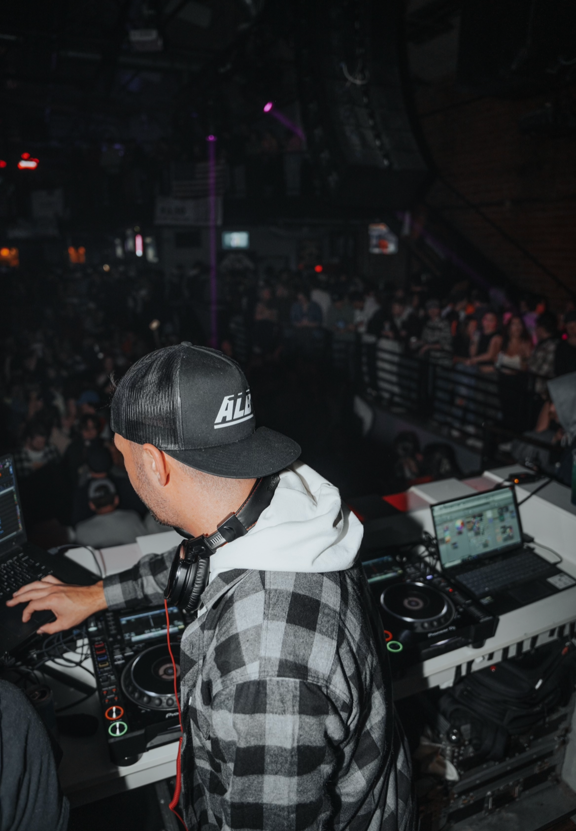 Alby performing at a nightclub with a crowd dancing in the background.