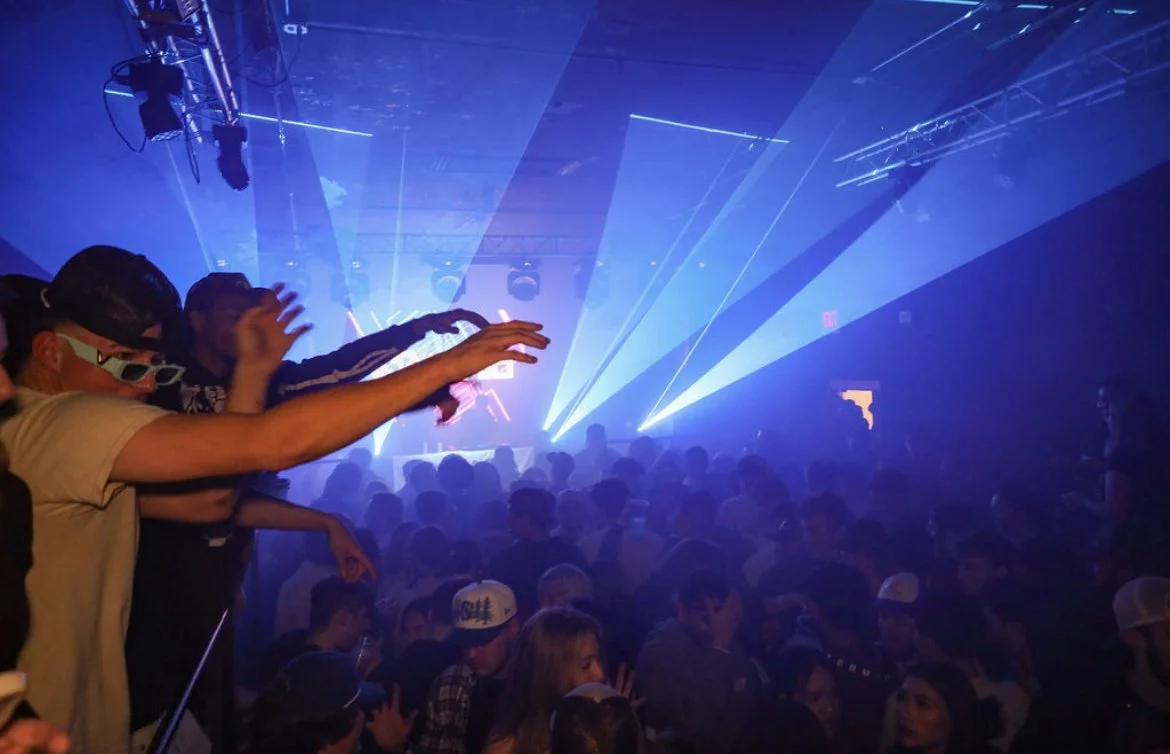 People dancing at a nightclub with blue laser lights and a dark atmosphere.