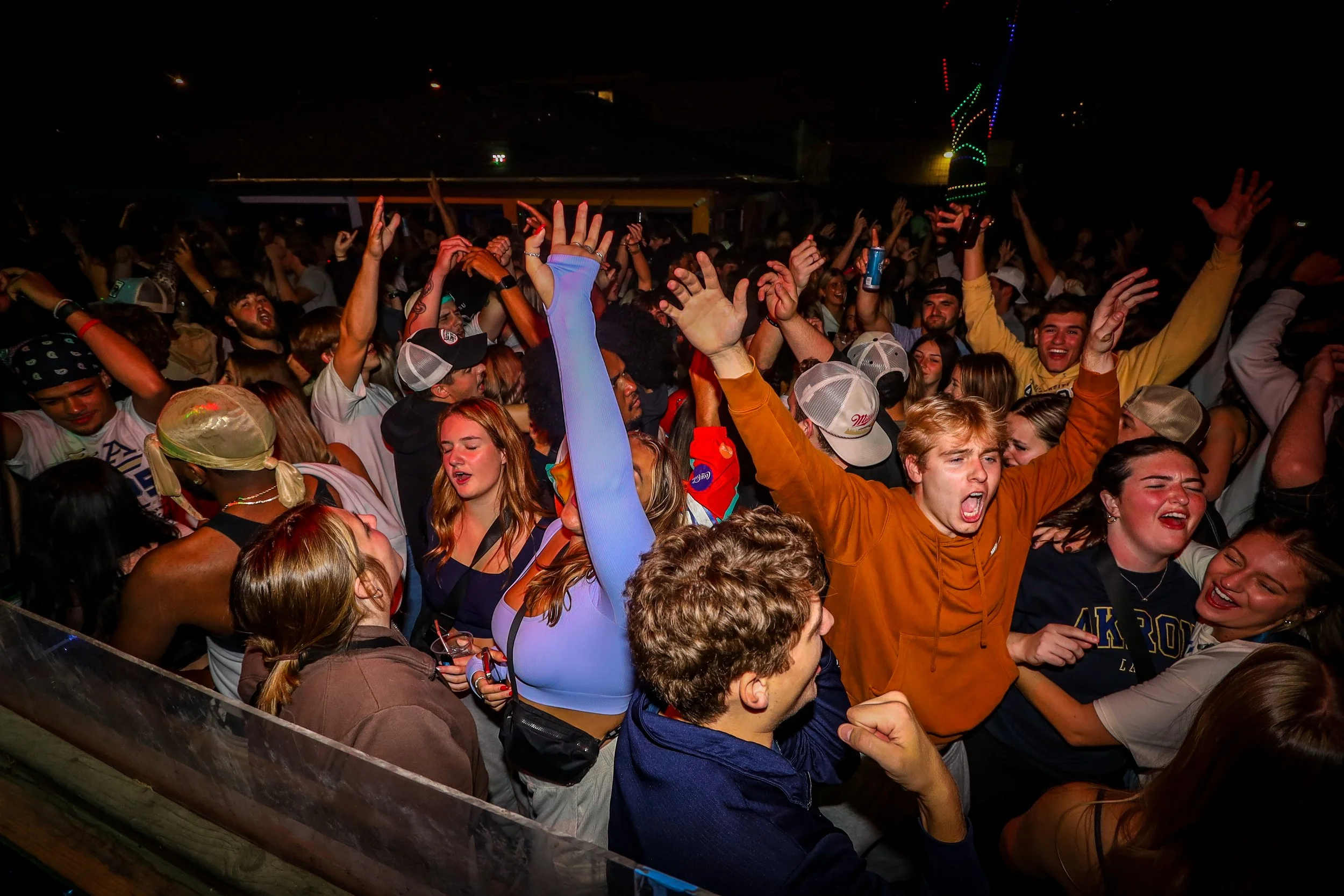Crowd of young people dancing and enjoying music at a night concert or festival, with some raising their hands and others singing.