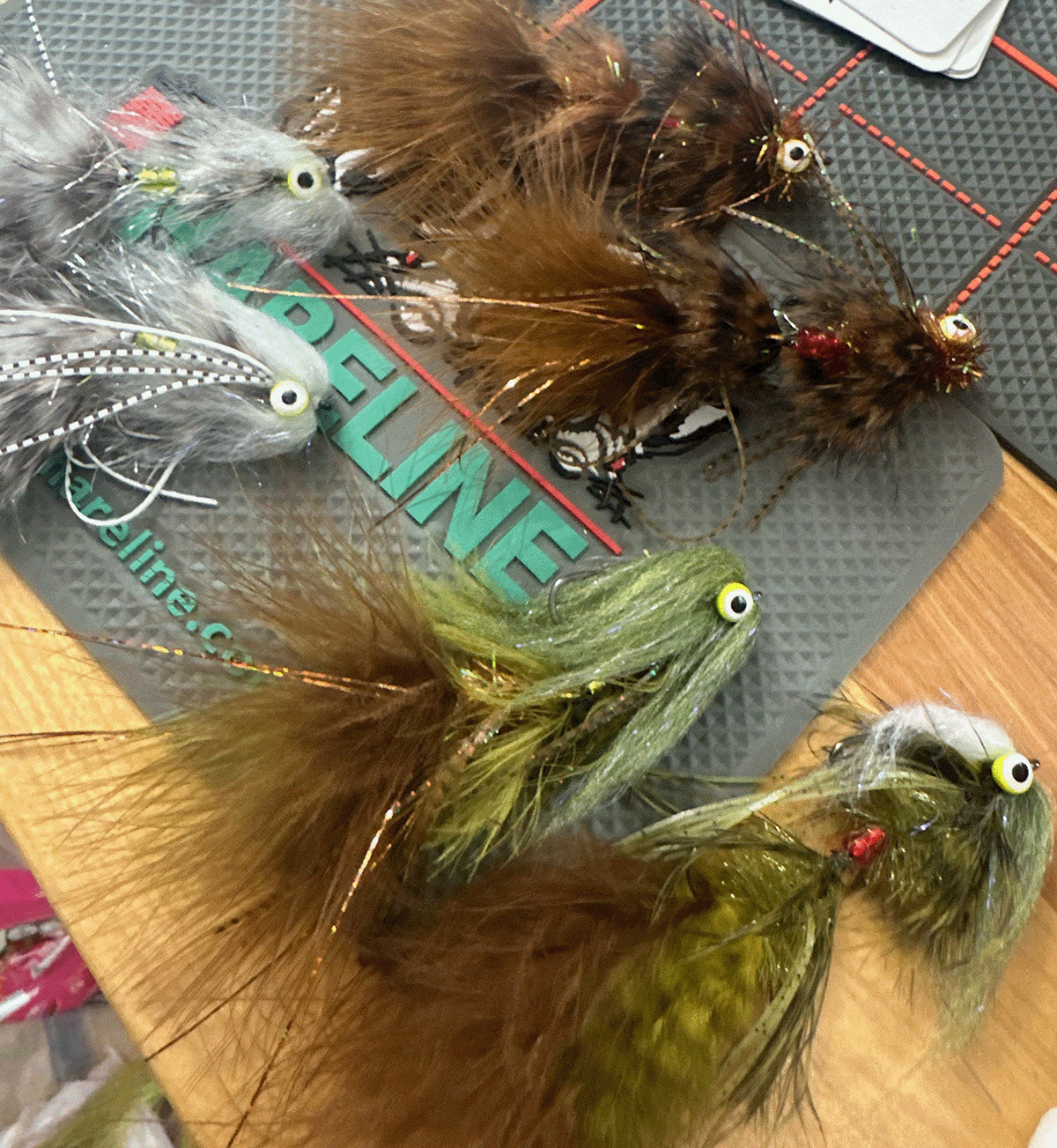 Multiple artificial fishing flies with colorful feathers and googly eyes laid out on a surface with fishing-related text.