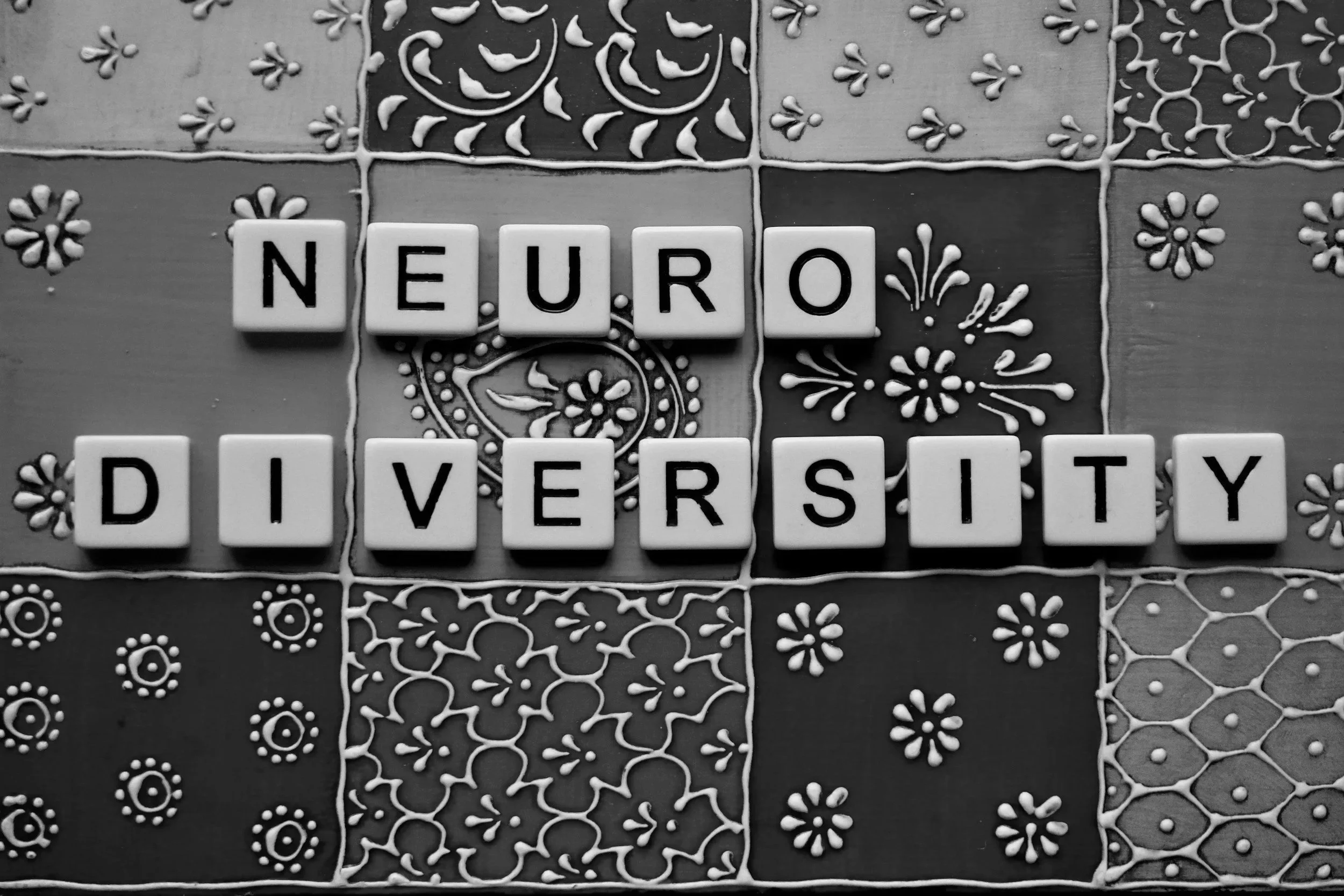 Black and white photo of letter tiles spelling 'NEURO DIVERSITY' on decorative patterned tiles.