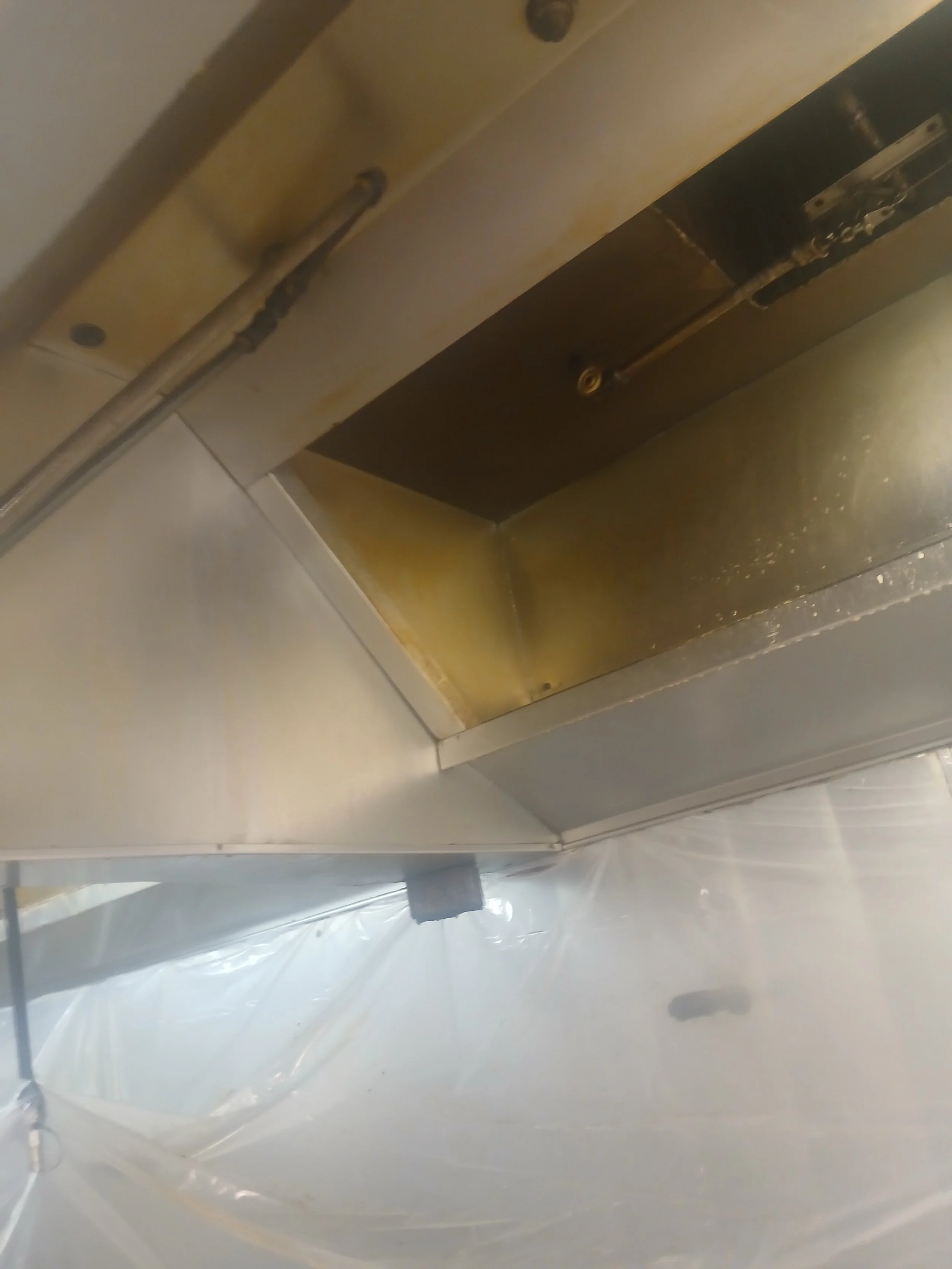 Close-up of industrial kitchen exhaust hood with ductwork and cleaning equipment.