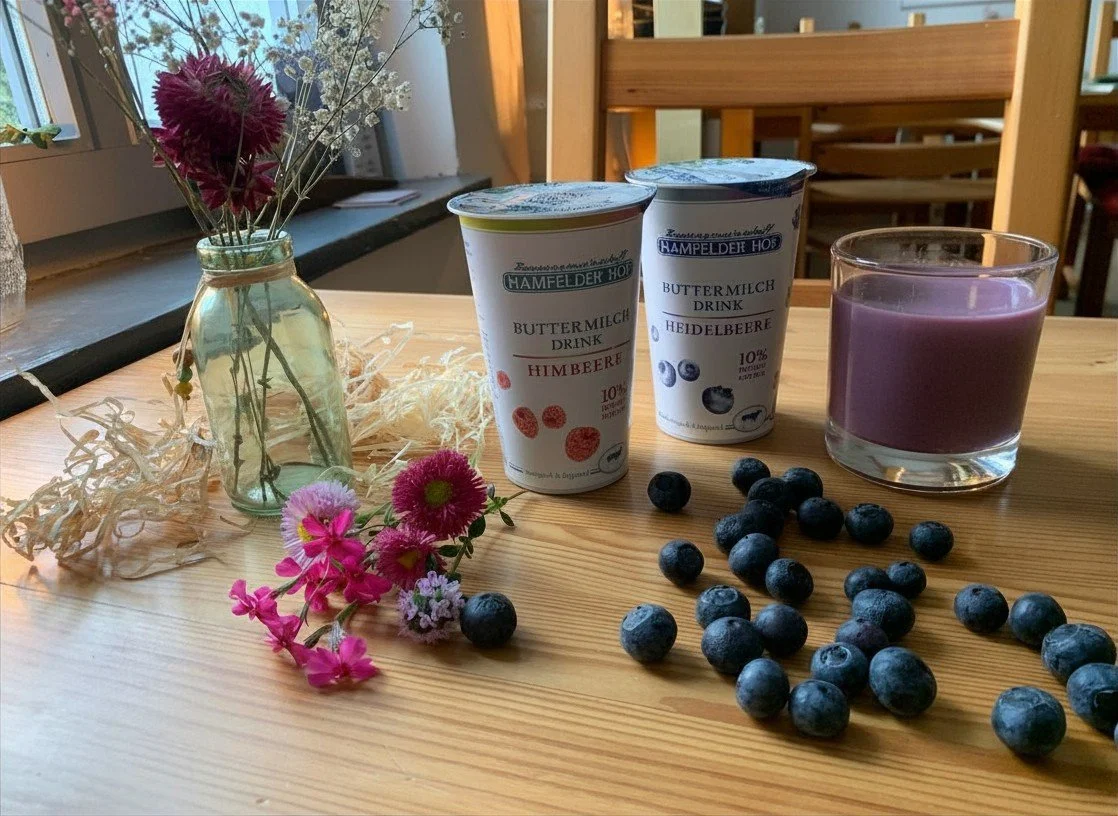 Ein Holztisch mit einer kleinen Vase voller bunter Blumen, zwei Becher mit Beeren-Joghurtdrinks, einem Glas mit einer violetten Flüssigkeit und frischen Heidelbeeren.