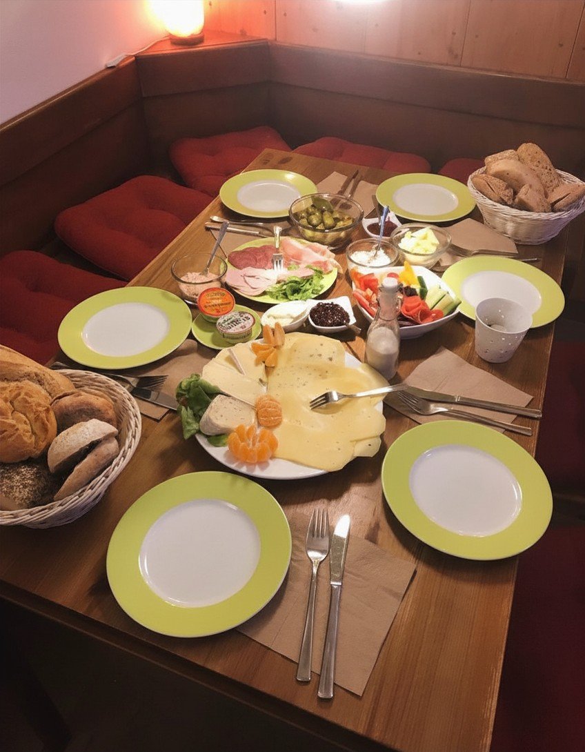 Ein Tisch gedeckt mit Frühstücksessen, darunter Käse, Wurst, Brot, Obst, Joghurt und Butter, mit grünen Tellern und Besteck.