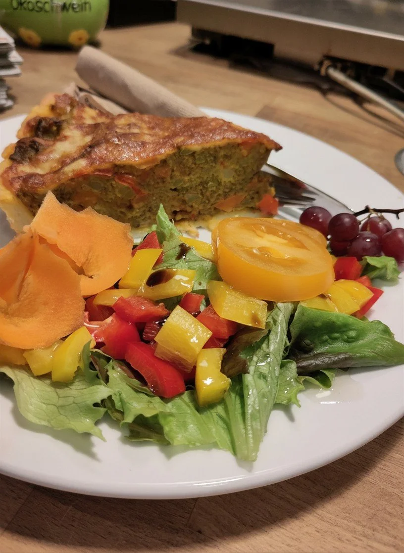 Gemischter Salat mit Tomaten, Paprika und Trauben, dazu eine Portion Gemüseauflauf auf einem weißen Teller.