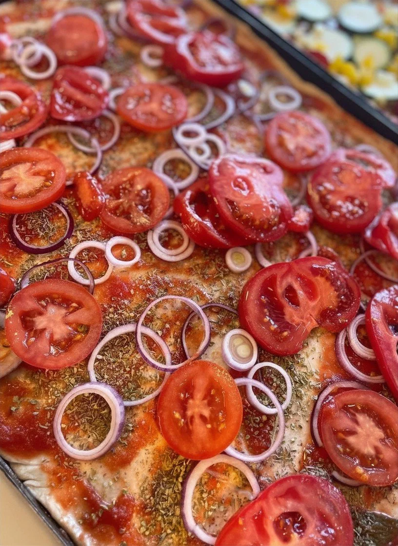 Nahaufnahme einer belegten Pizza mit Tomatenscheiben und roten Zwiebelringen.
