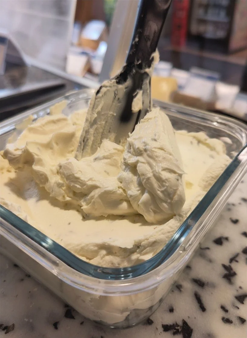 Eismasse in einer Glasschale mit Eiskelle, wahrscheinlich Vanilleeis in einer Eisdiele