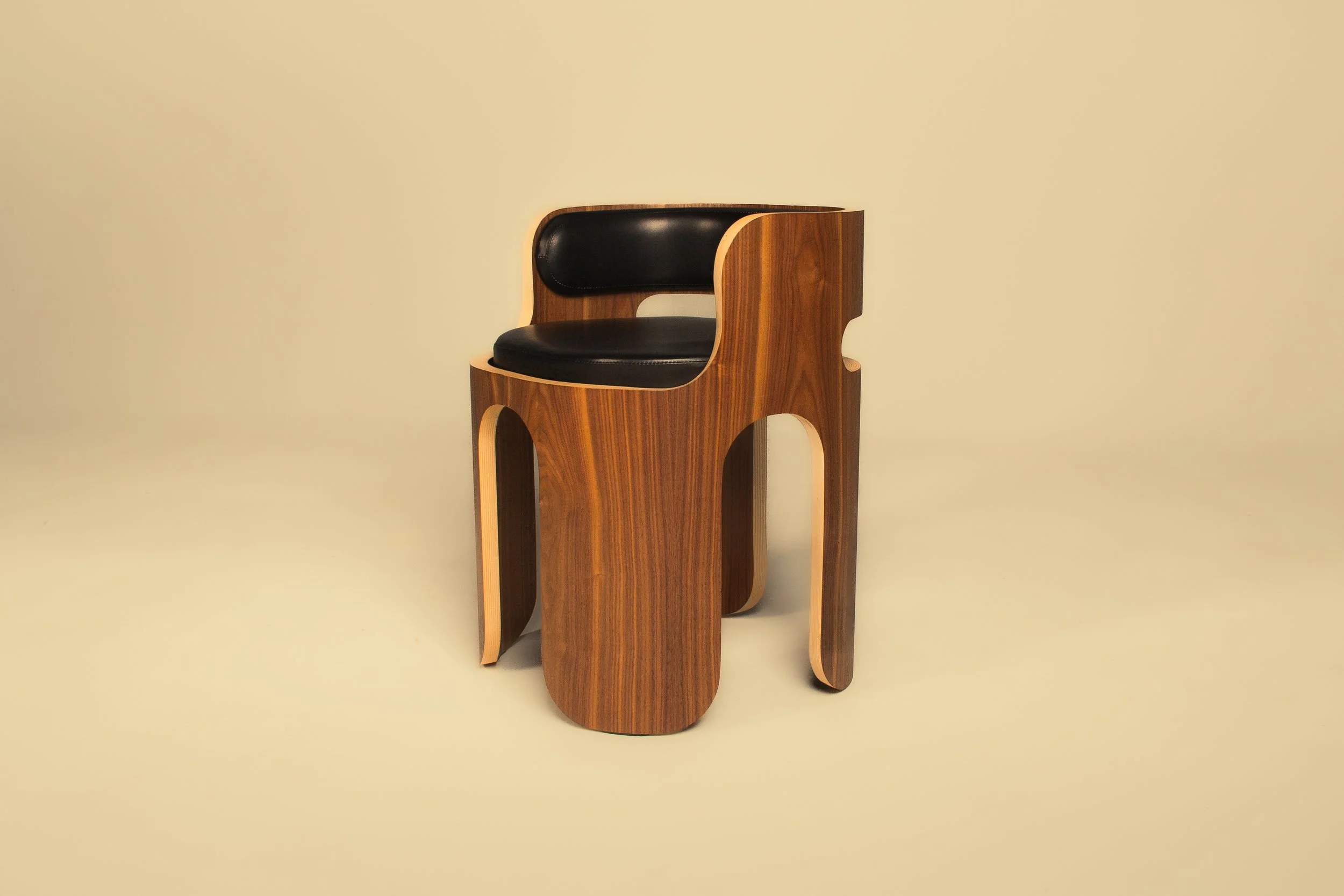 A modern wooden chair with curved design, black cushion on the seat and backrest, set against a plain beige background.
