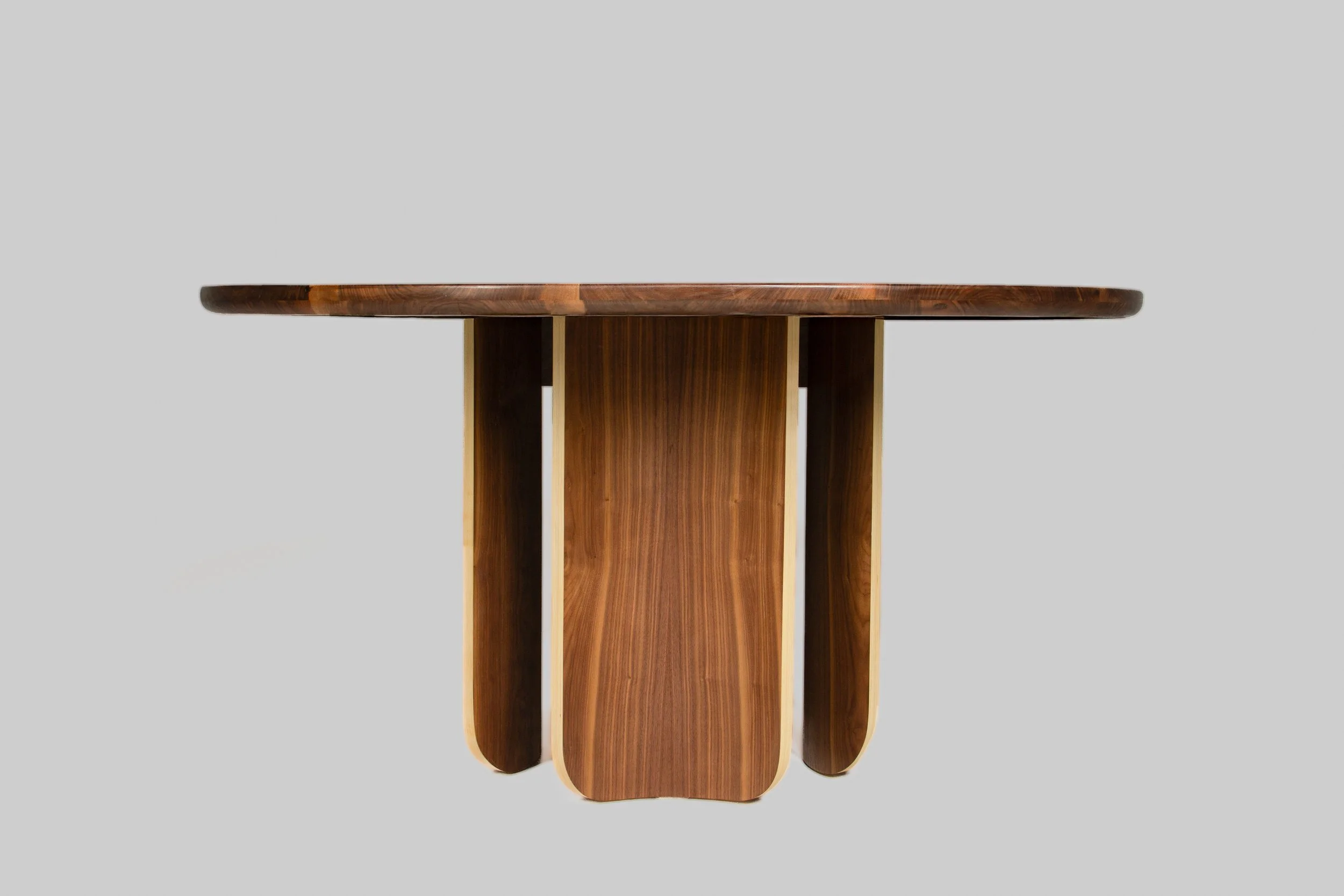 A wooden table with a rounded top and a pedestal base made of curved wooden panels, set against a plain gray background.
