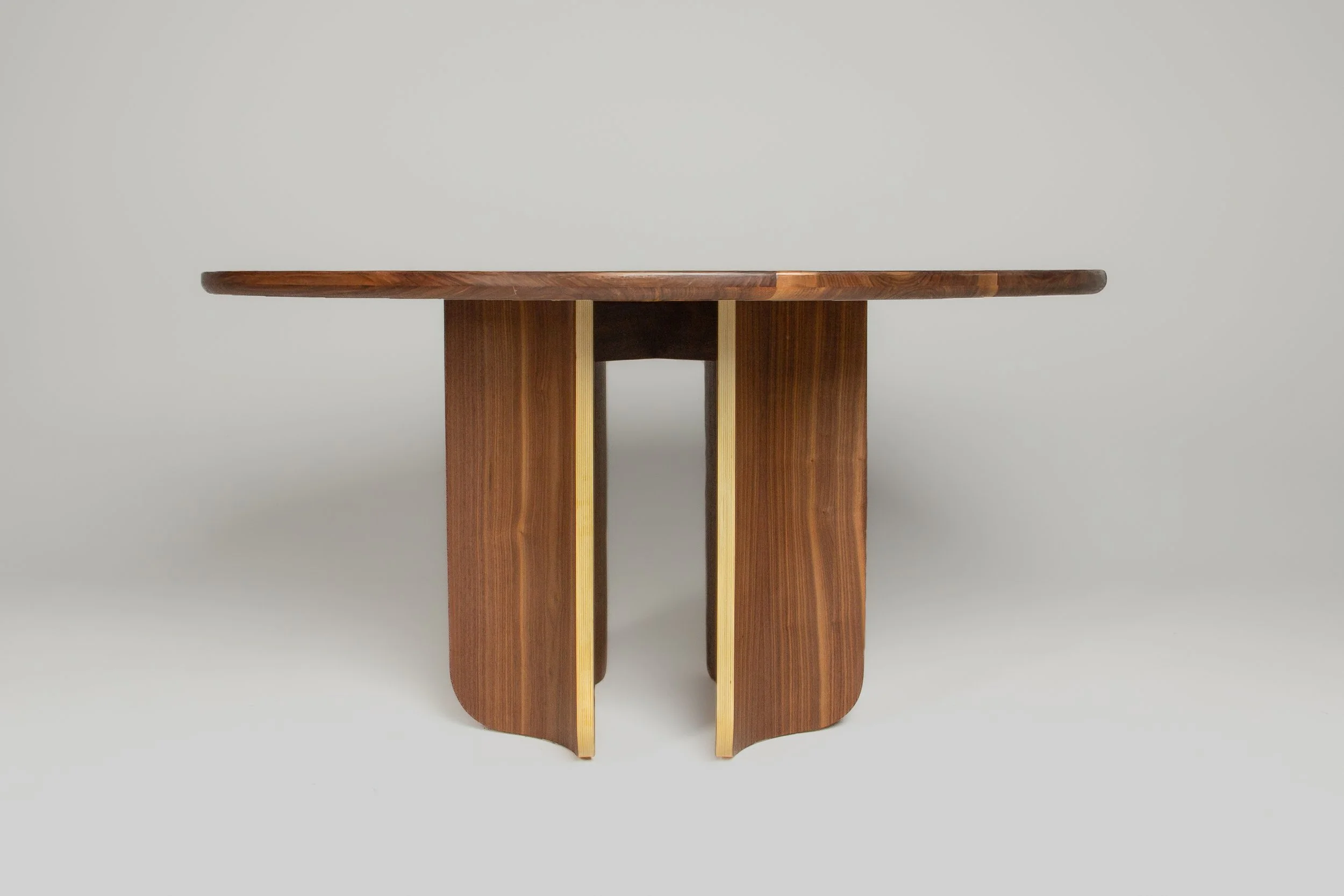 A modern wooden table with a round top and curved legs against a plain light grey background.