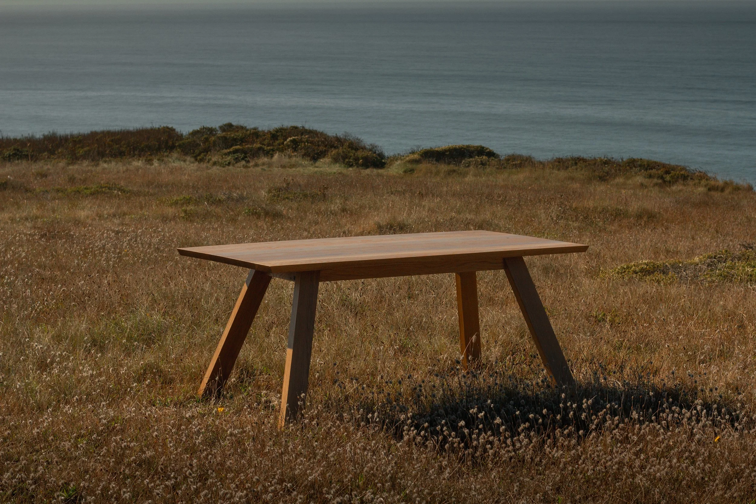 A wooden table situated on a grassy field near the coast, with the ocean visible in the background.