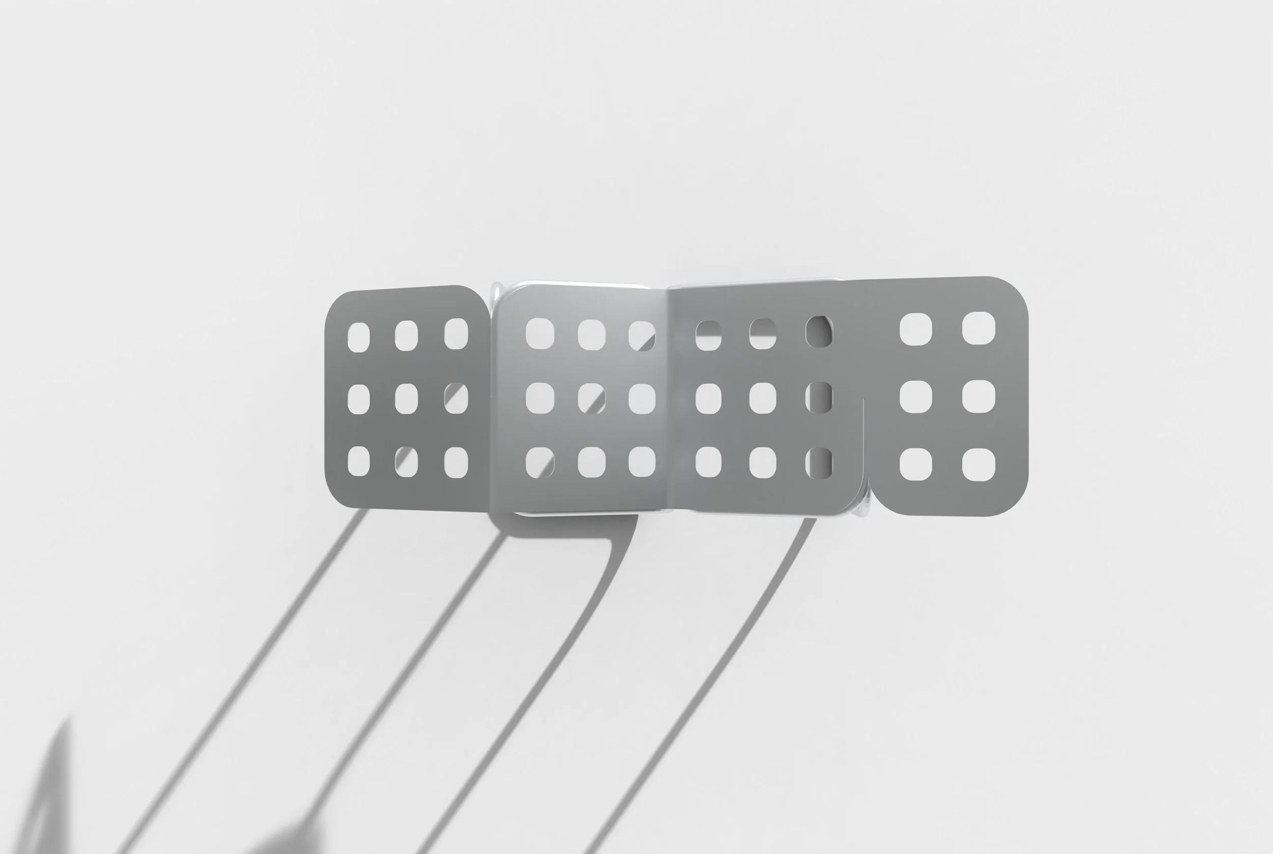 A minimalist white metal domino display with three dominoes casting shadows on a white background.