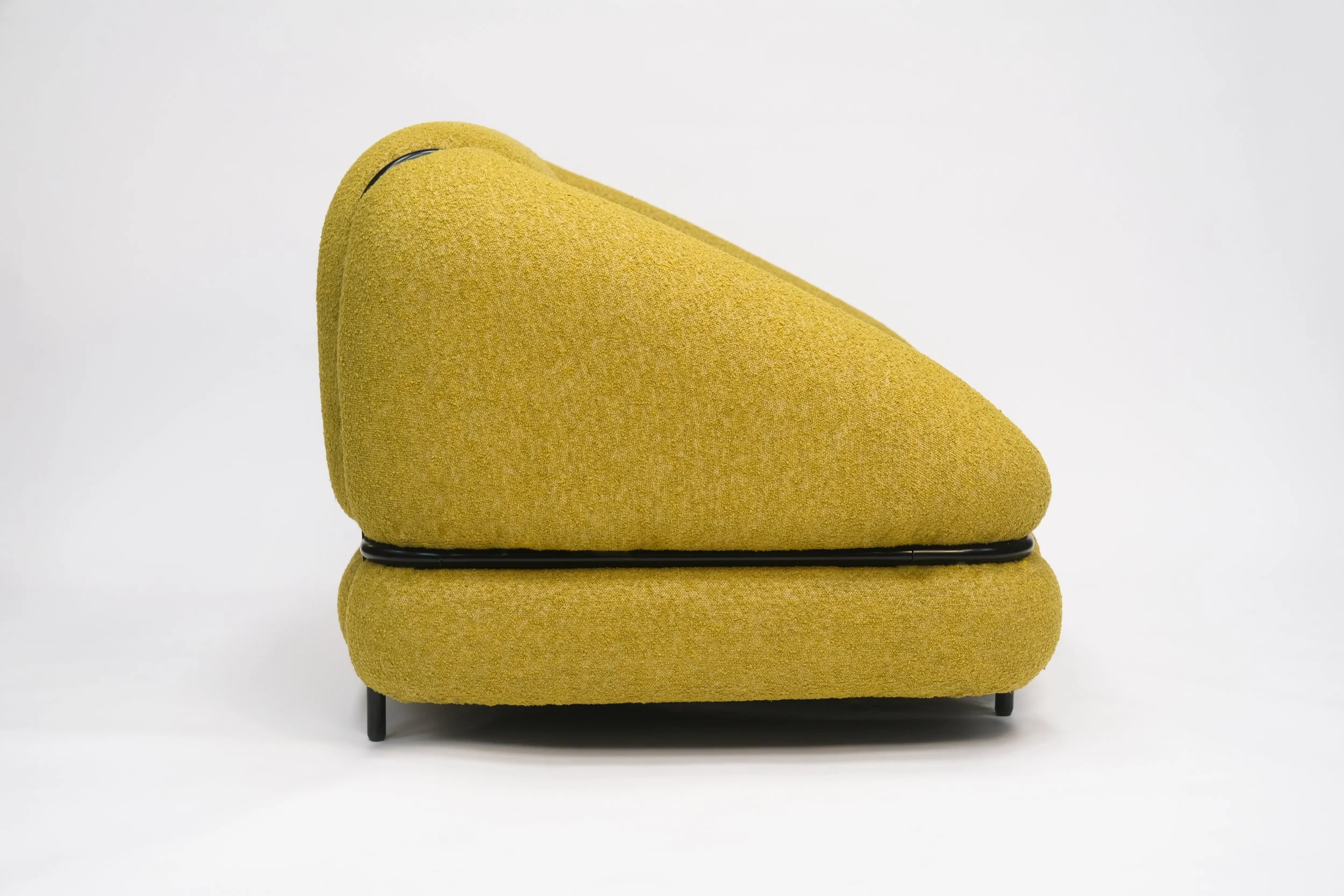 A modern mustard yellow upholstered lounge chair with a curved back and black metal legs, set against a plain white background.
