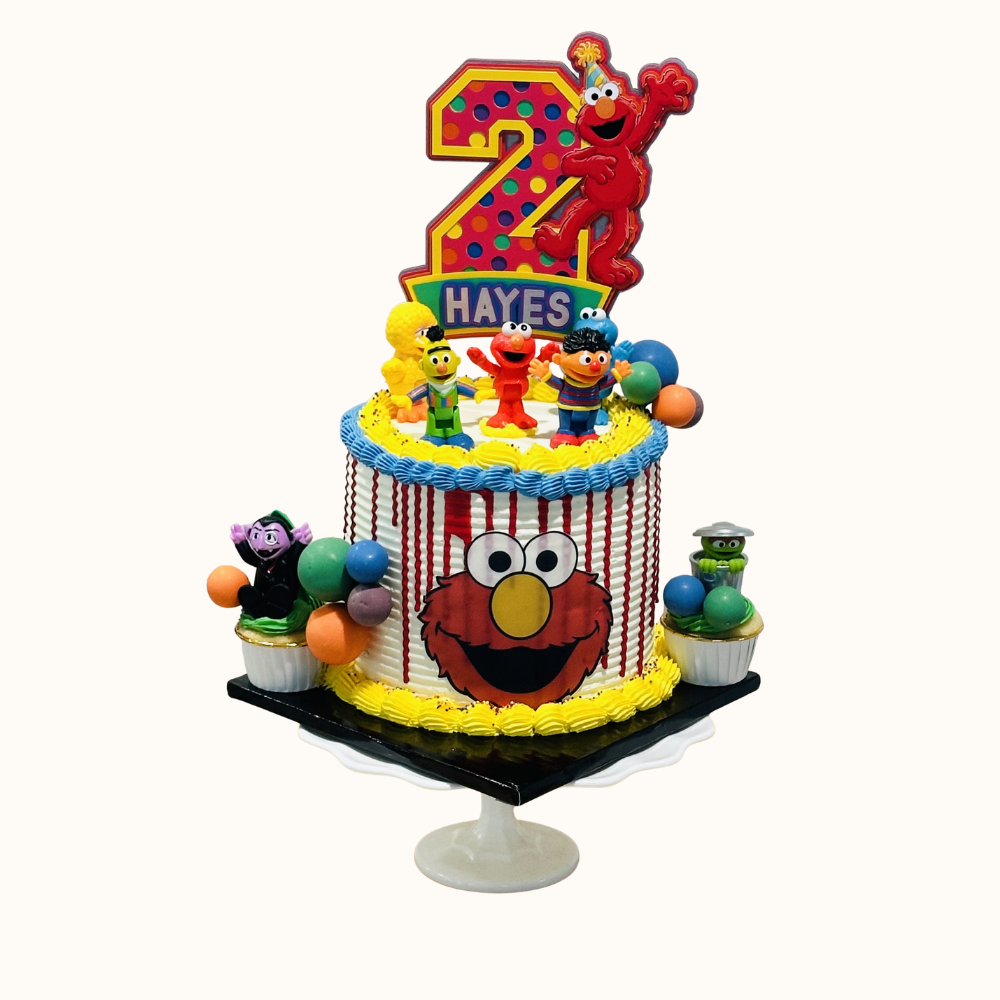A white birthday cake with light blue, yellow and red icing features Sesame Street characters: Elmo, Count von Count, Big Bird, Bert, Ernie, and Oscar the Grouch, and a 2 topper with Elmo in a birthday hat for a child named Hayes.