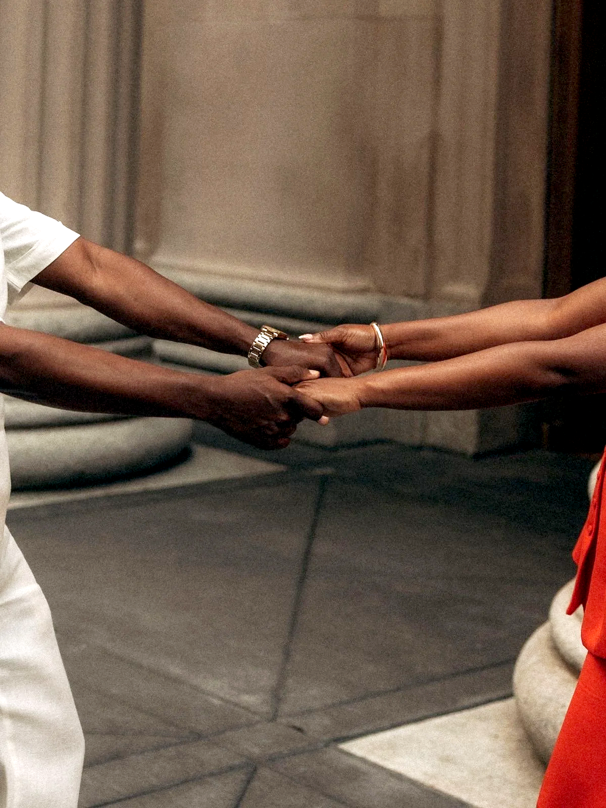 Two people holding hands, one wearing a watch, in an indoor setting.