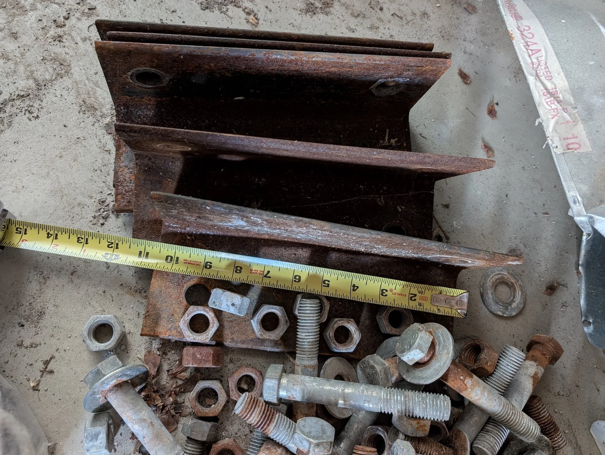 Removed steel brackets, bolts, and nuts beside a measuring tape.
