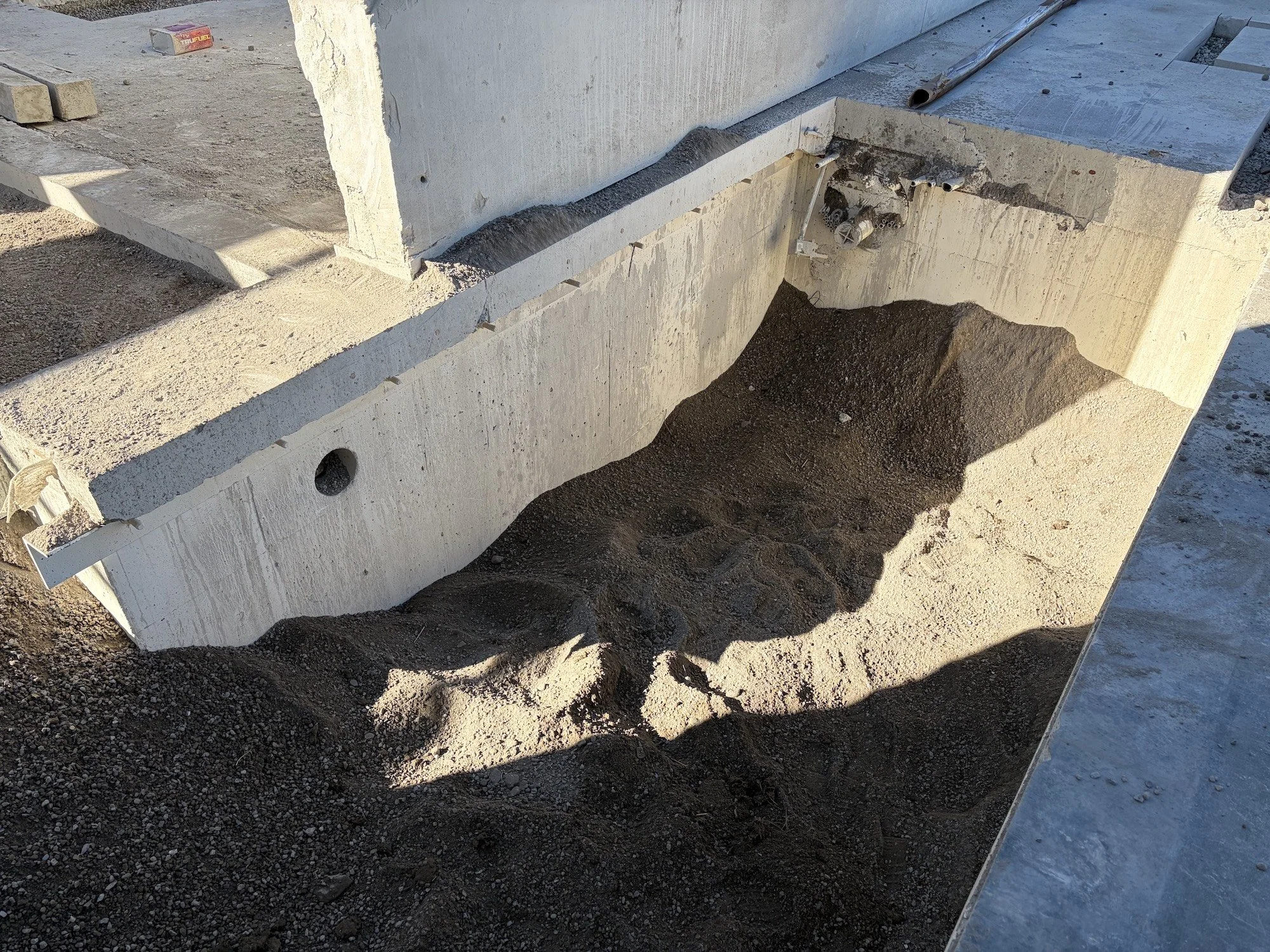 Excavated gravel beneath a retained wall and concrete foundation.