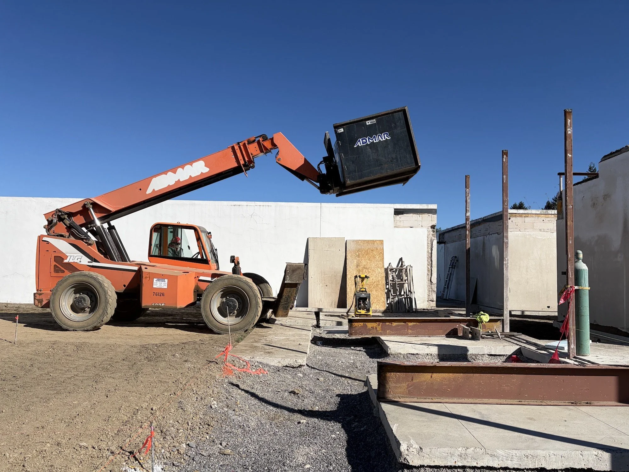 Orange telescopic handler beside retained walls and exposed steel framing.