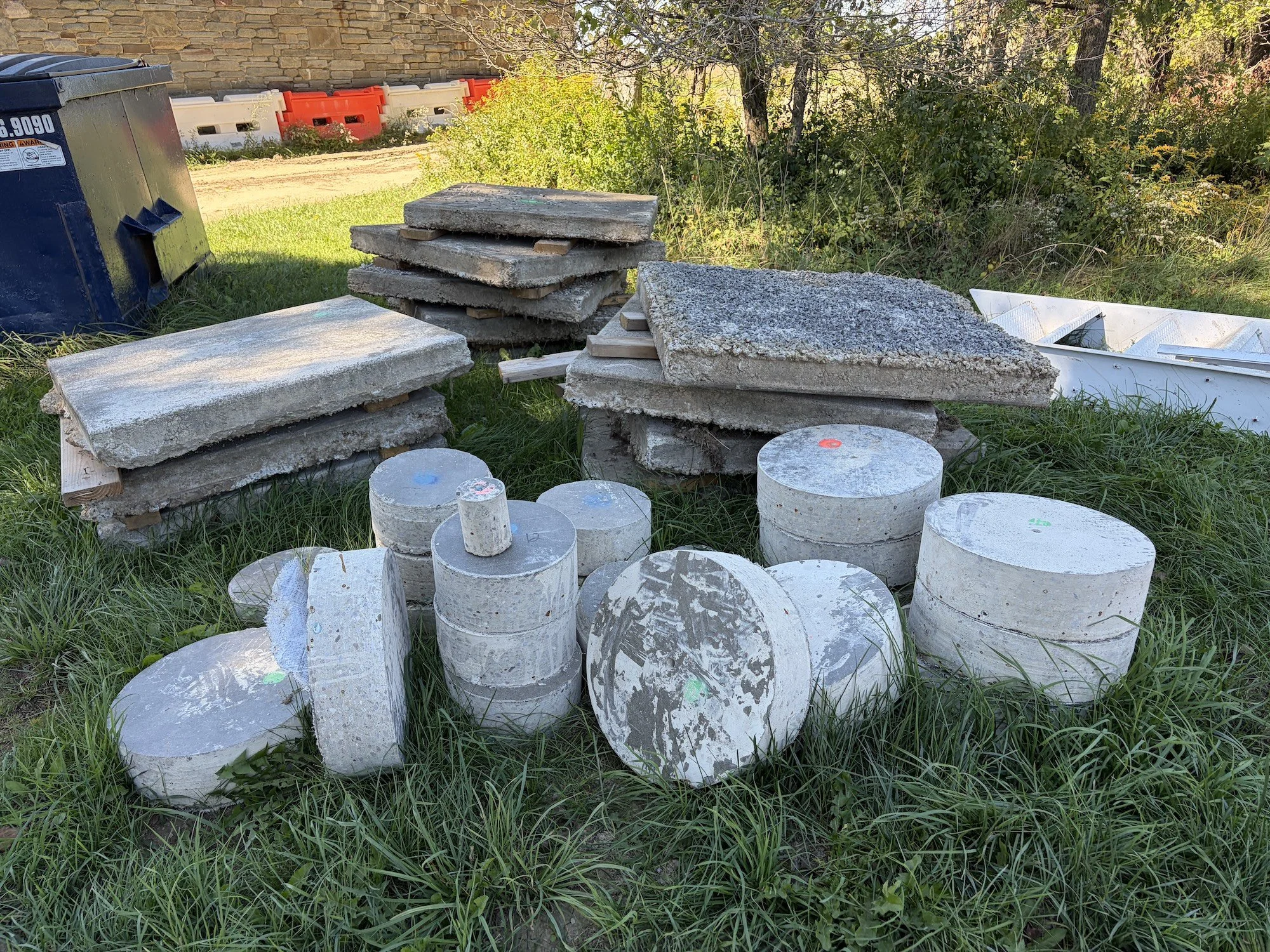 Stacked concrete slabs and cylindrical concrete cores on grass.