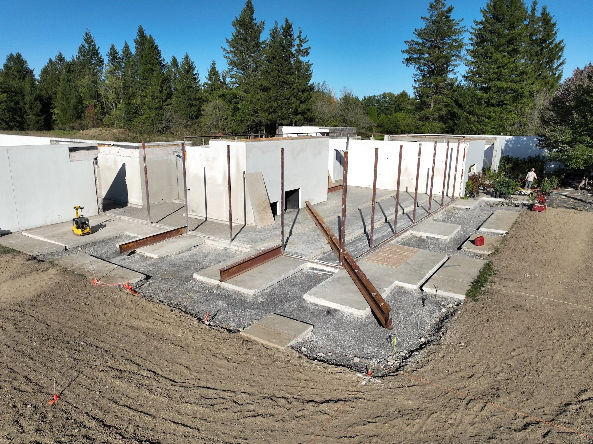 Roofless building with retained white walls, steel columns, and cut concrete slabs.