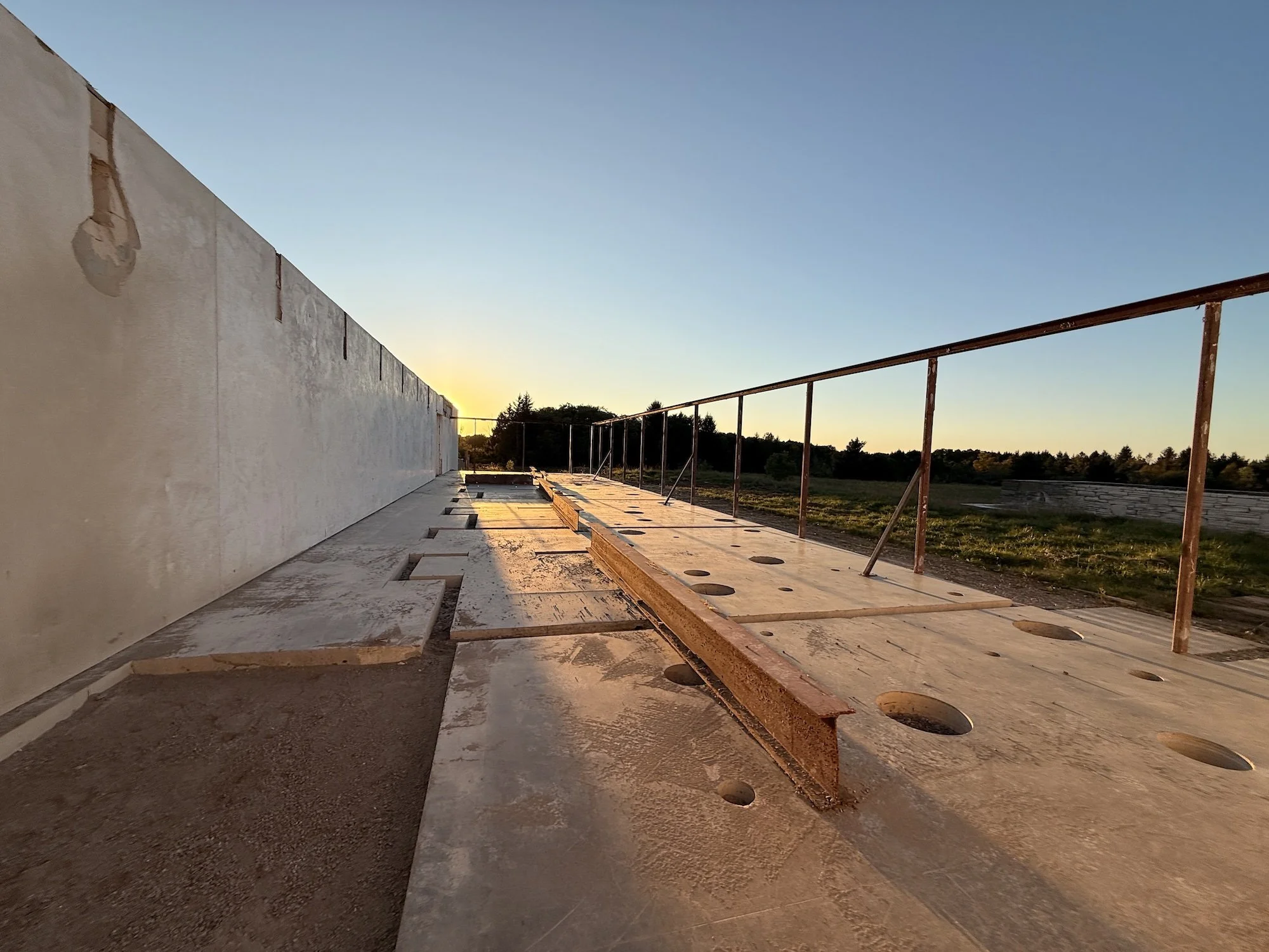 Sunset across Fairlawn’s exposed concrete floor, steel framing, and retained white wall.